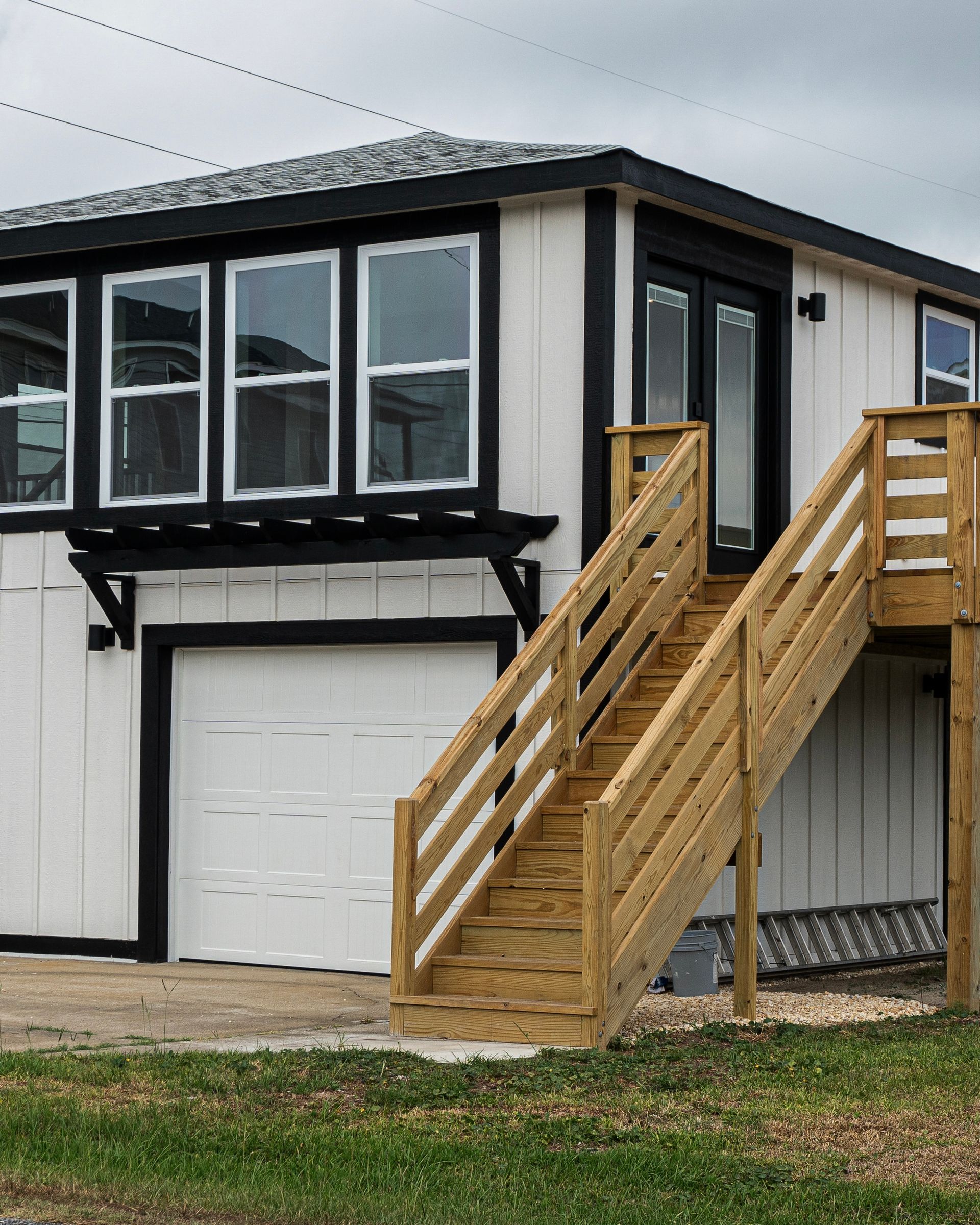 Two-story white building with black trim, wooden stairs leading to the second floor, and a garage door.