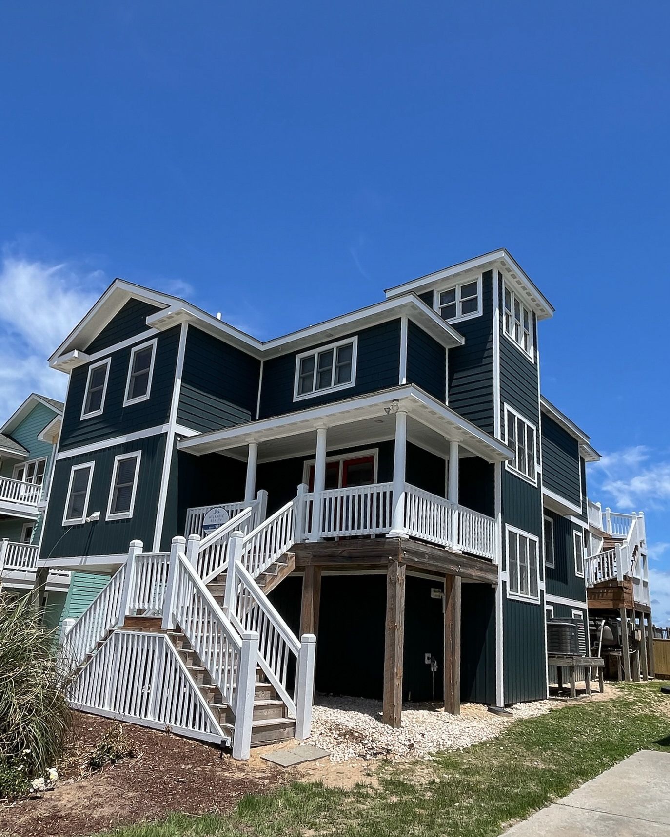 Three-story teal house with white trim, balcony, and staircase under a blue sky.