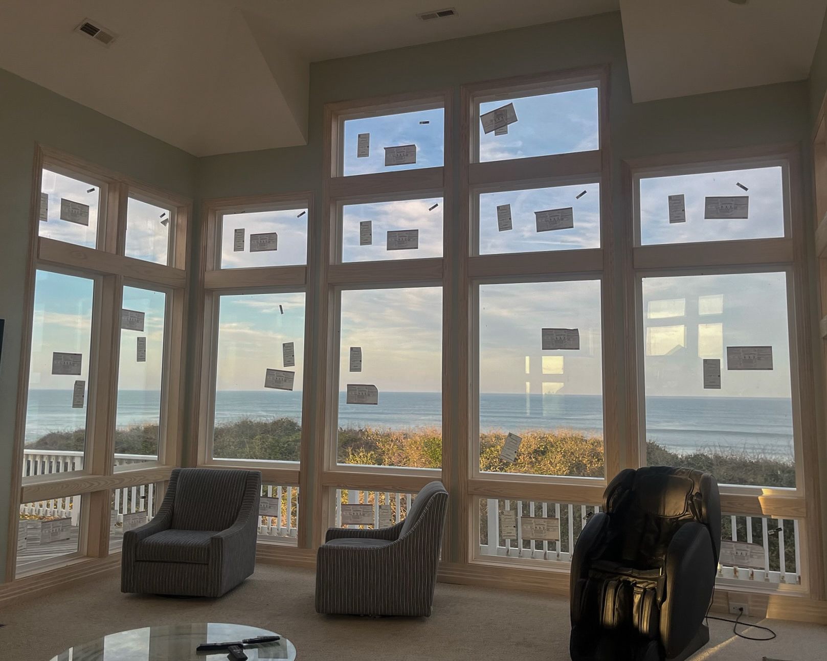 Living room with large windows overlooking the ocean. Two armchairs and a recliner are inside.