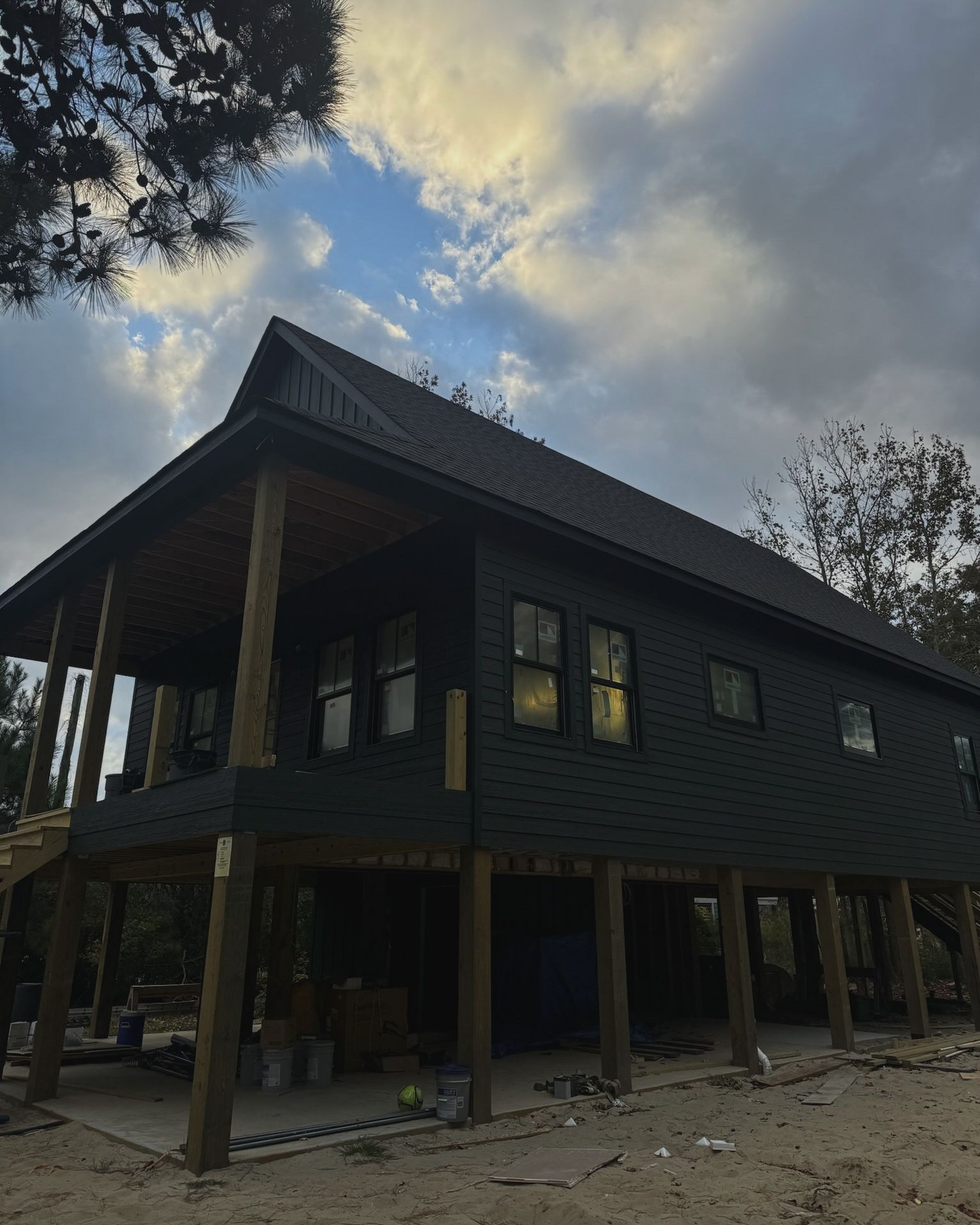 Dark green house on stilts under a cloudy sky.