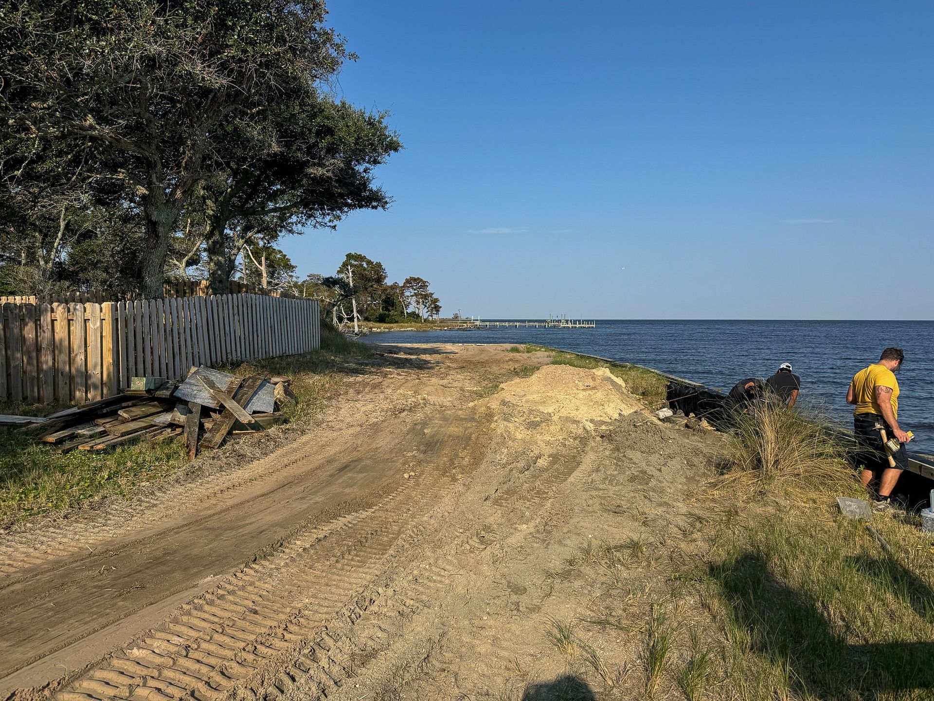 Beach scene with dirt, water, and a person. Brown dirt path, blue water, person in yellow shirt.