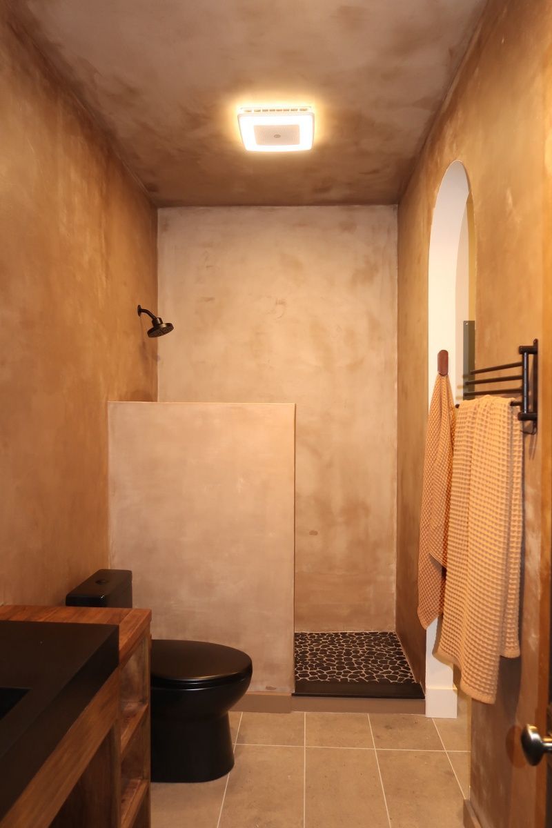 Bathroom with tan walls, black toilet, and shower. Two orange towels hang on a rack.