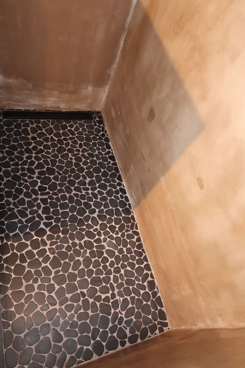Shower stall with black pebble tile floor and tan walls.