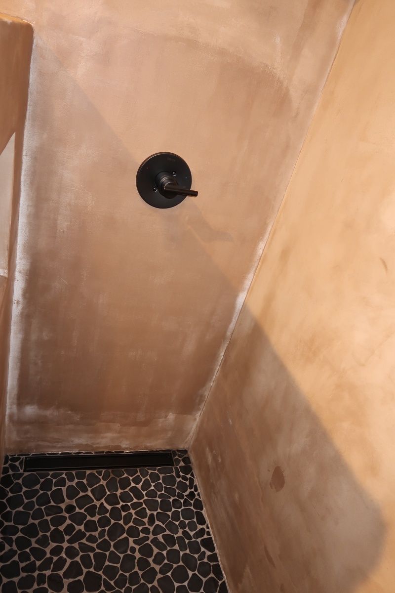 Shower with tan walls, black pebble floor, and black faucet.