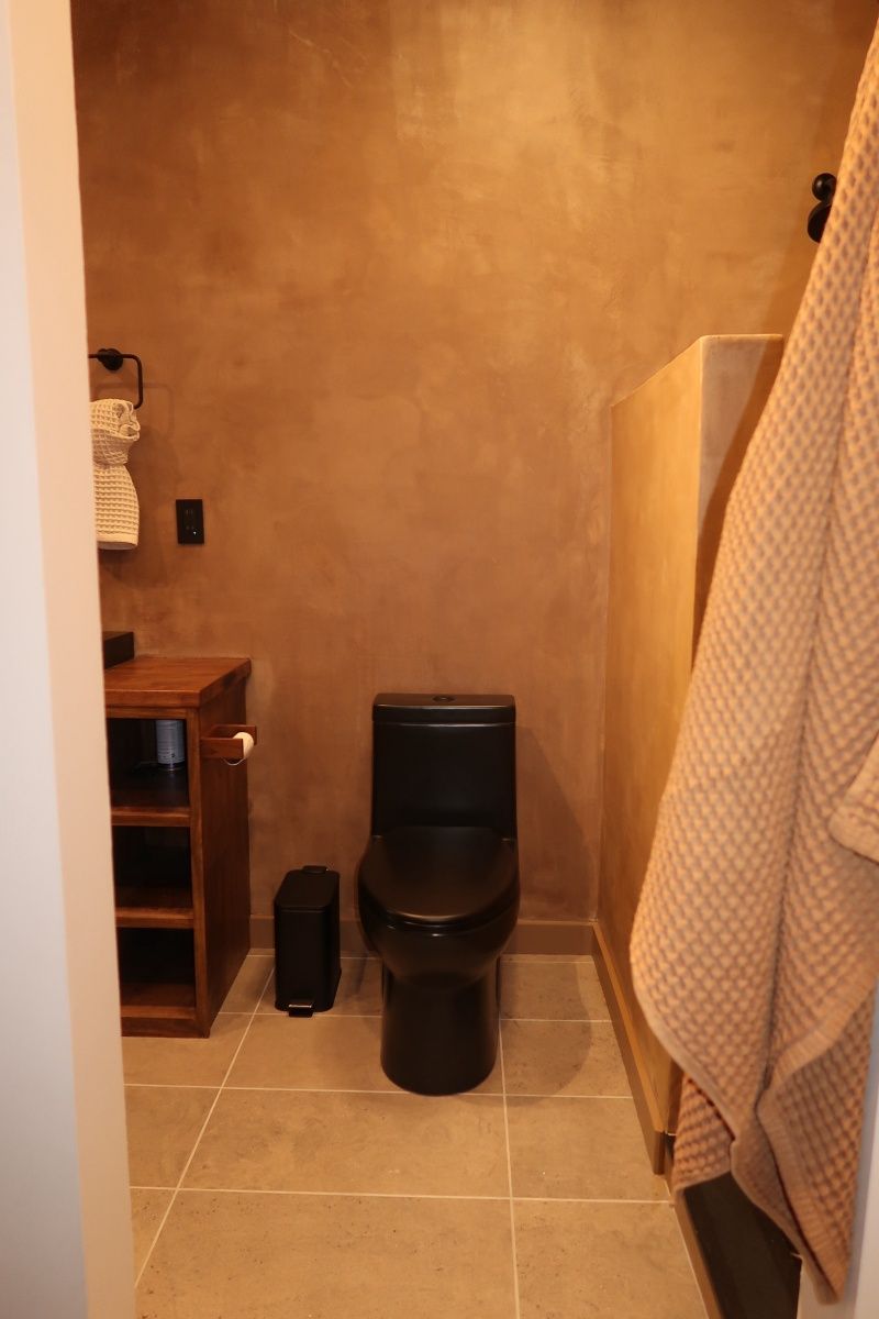 Black toilet in a brown-walled bathroom with wooden cabinets and a hanging beige towel.