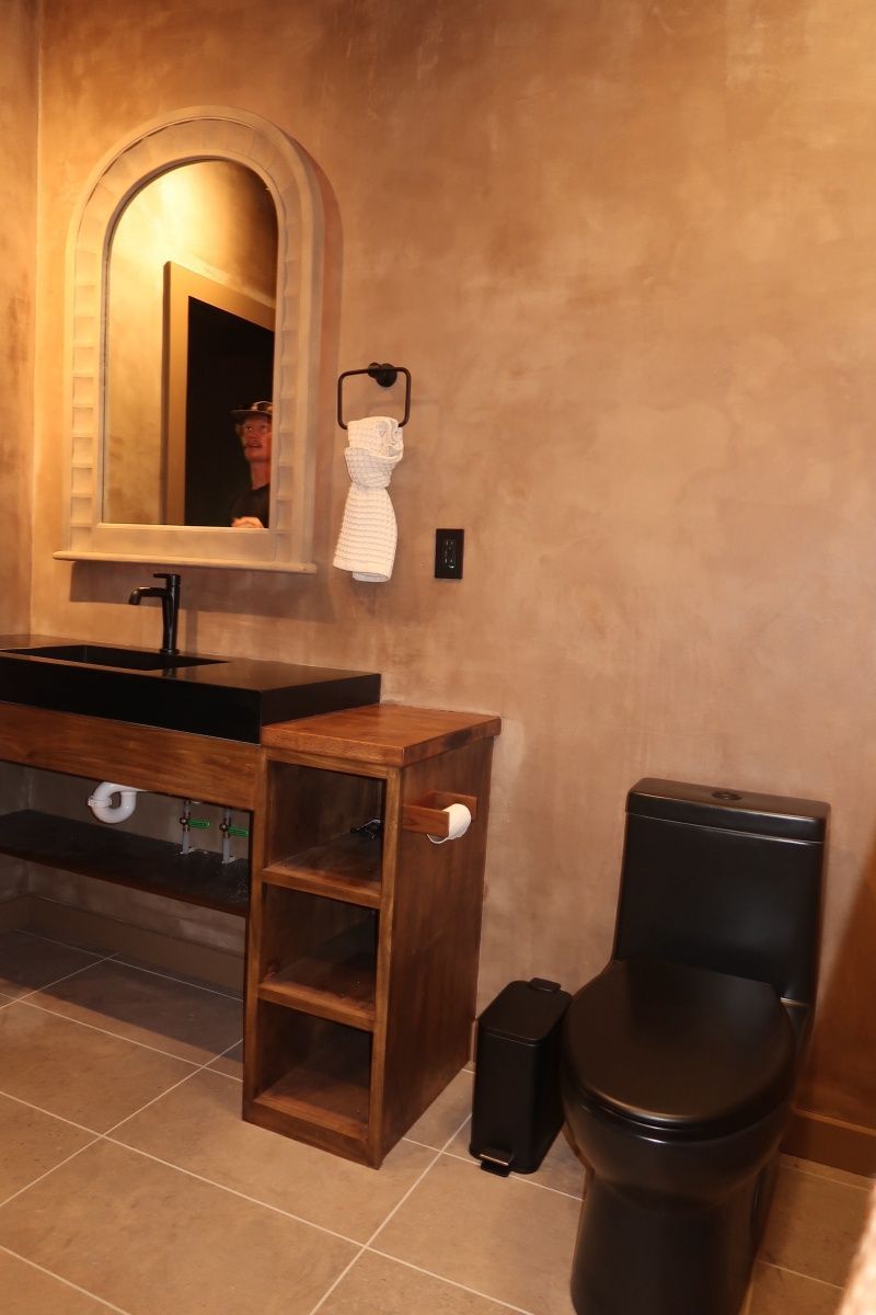 Bathroom with black toilet, sink, and wooden cabinet, featuring an arched mirror.