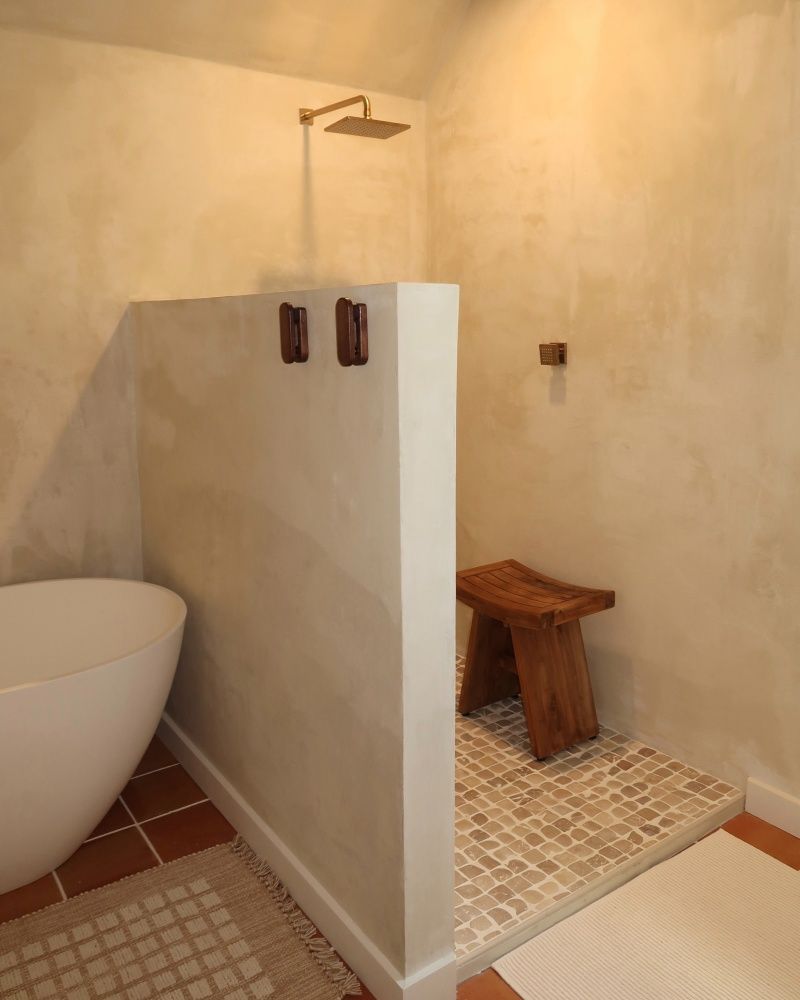Shower stall with wooden stool, stone floor, and beige walls.