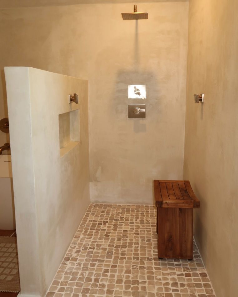 Neutral-toned shower with a wooden bench, tiled floor, and recessed shelving. Wall-mounted shower head and fixtures.
