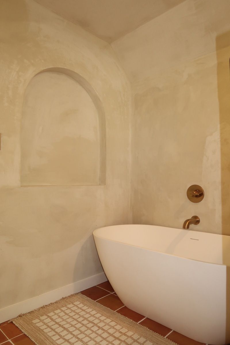 Bathroom with a white, oval-shaped tub, built-in arched wall niche, and terracotta-colored floor tiles.