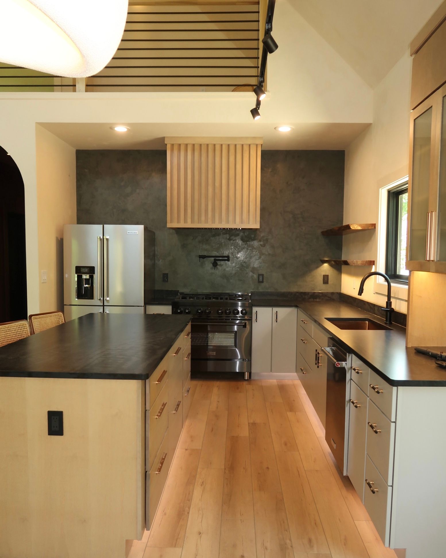Modern kitchen with island, stainless steel appliances, wood cabinets, and dark countertops.