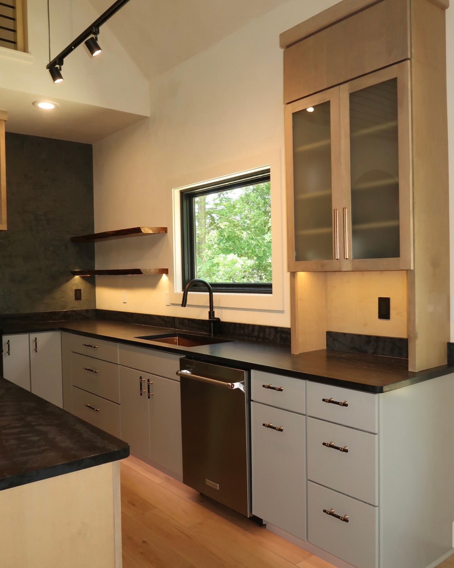 Modern kitchen with gray cabinets, black countertops, stainless steel appliances, and a window.
