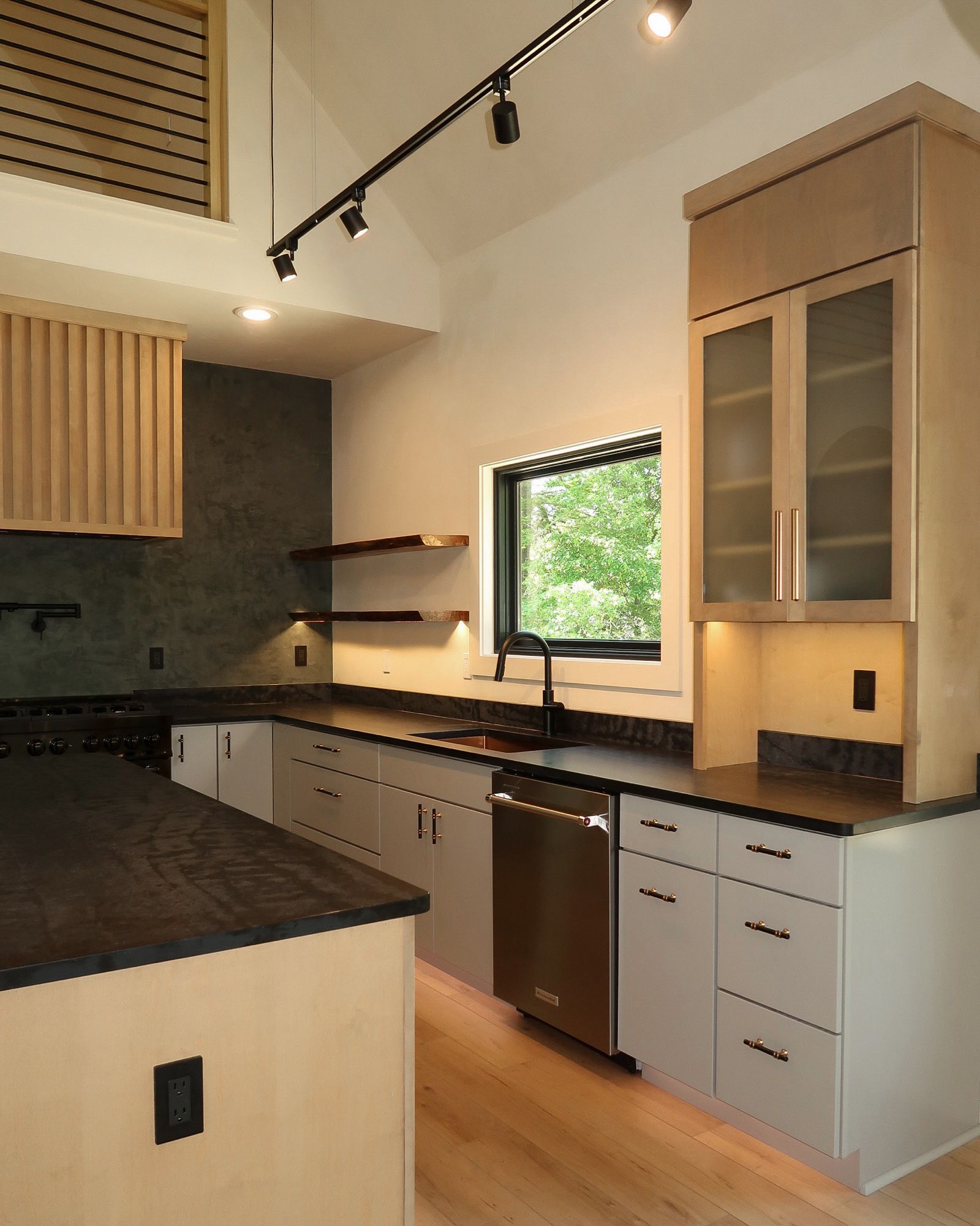 Modern kitchen with light wood cabinets, black countertops, and stainless steel appliances.