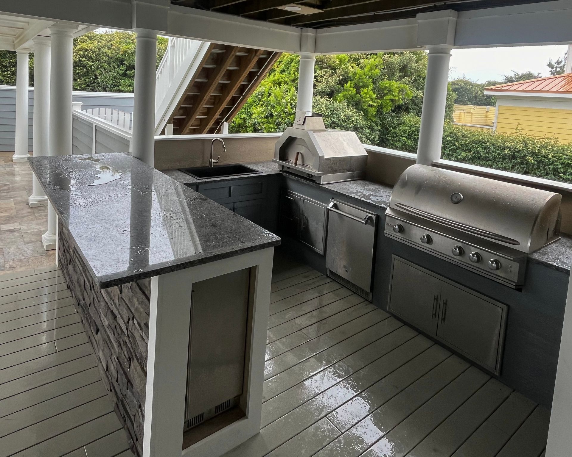 Outdoor kitchen with granite countertops and stone accents, under a covered patio.