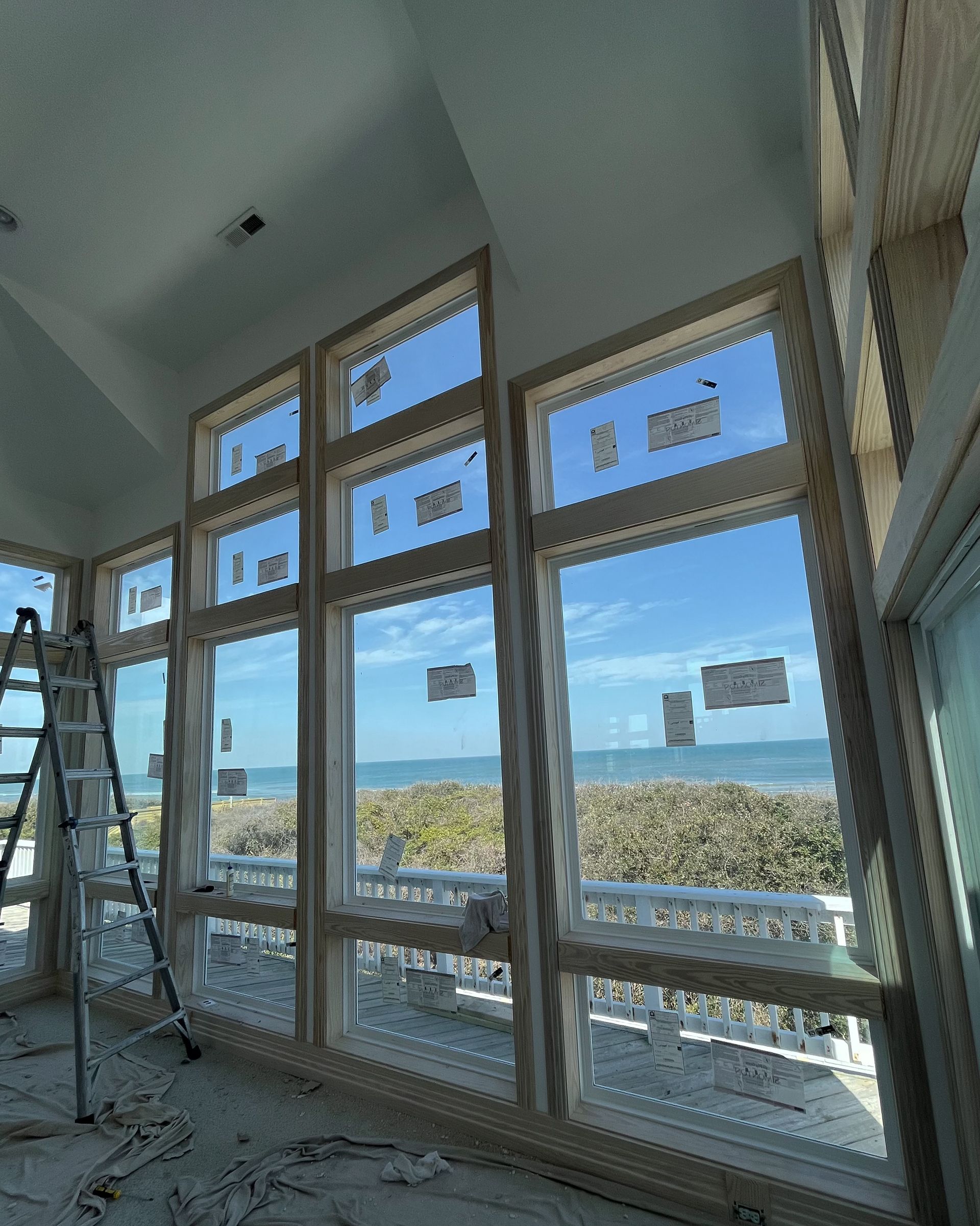 Interior view of a room with large windows overlooking a beach. A ladder rests on the left.