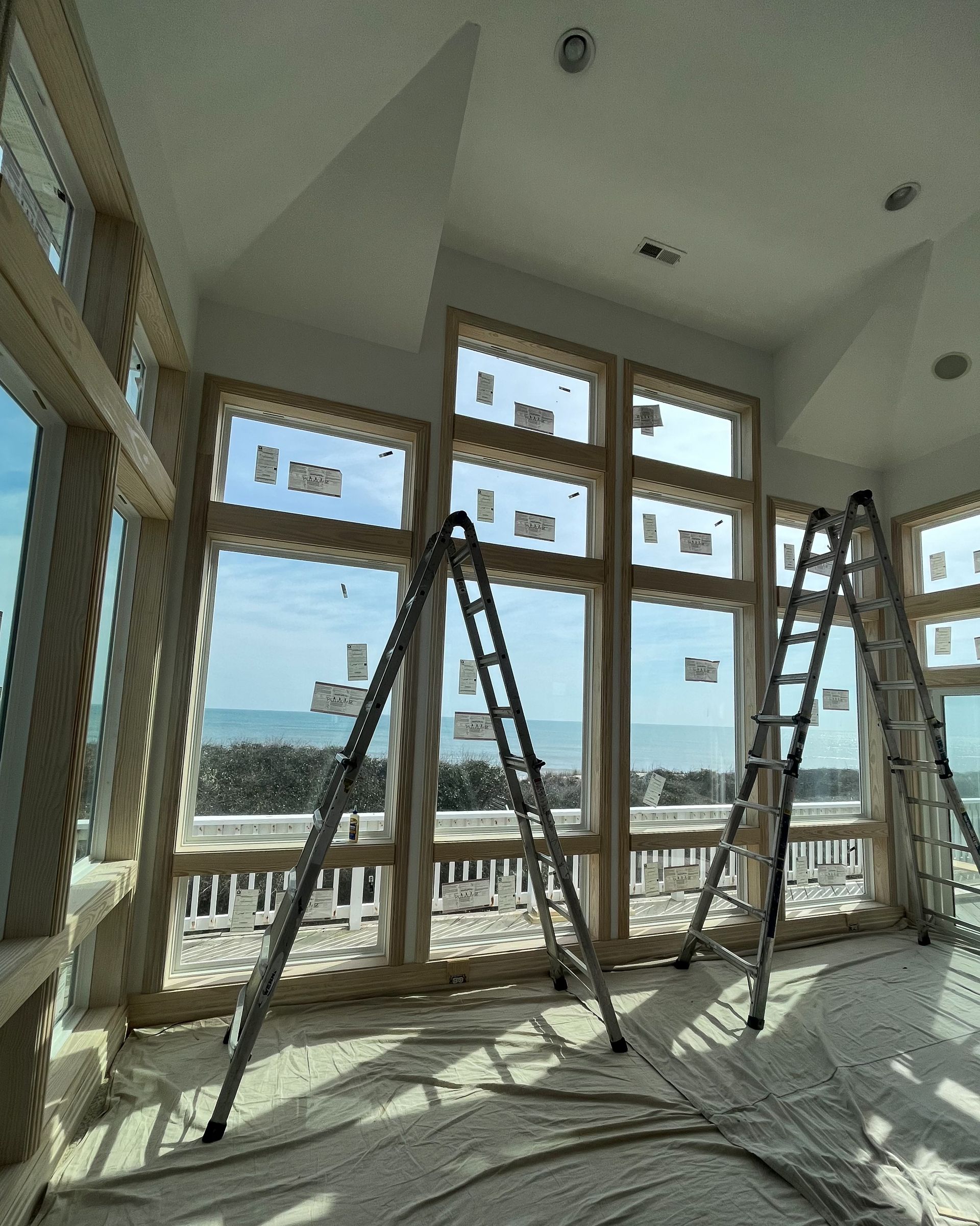 Interior view of room with tall windows, three ladders, and a coastal view.