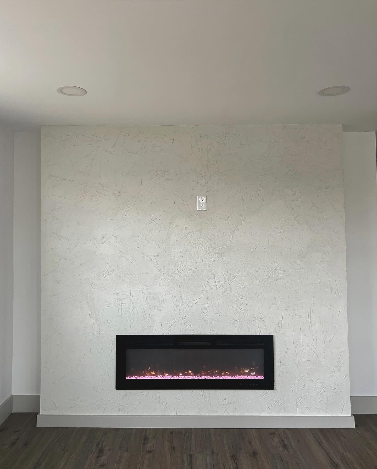 Electric fireplace with a glowing flame in a textured white wall.