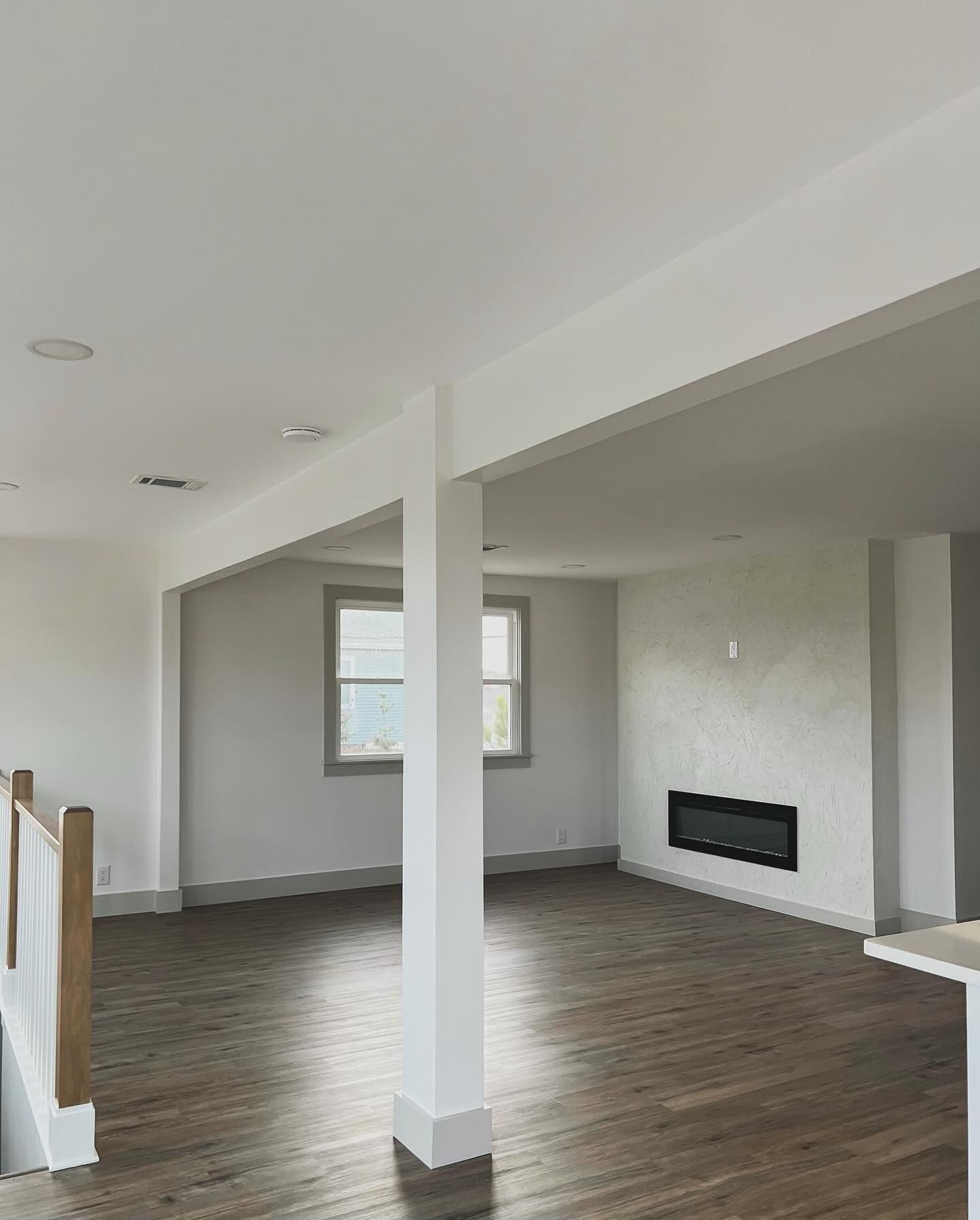 Empty living room with white walls, dark wood floors, and a fireplace.