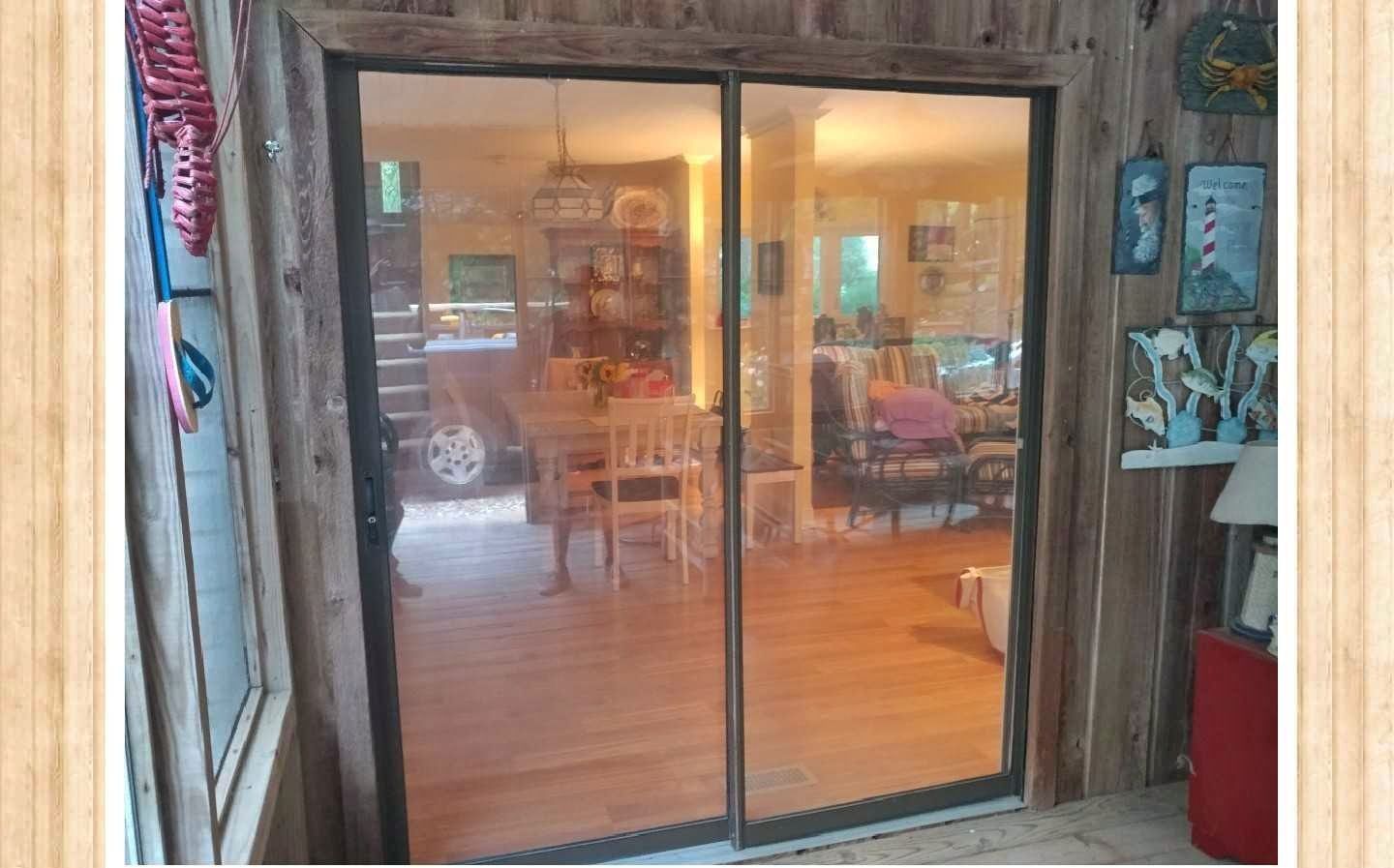 Sliding glass doors reflecting a dining room with a table, chairs, and people; set in a wooden-paneled frame.