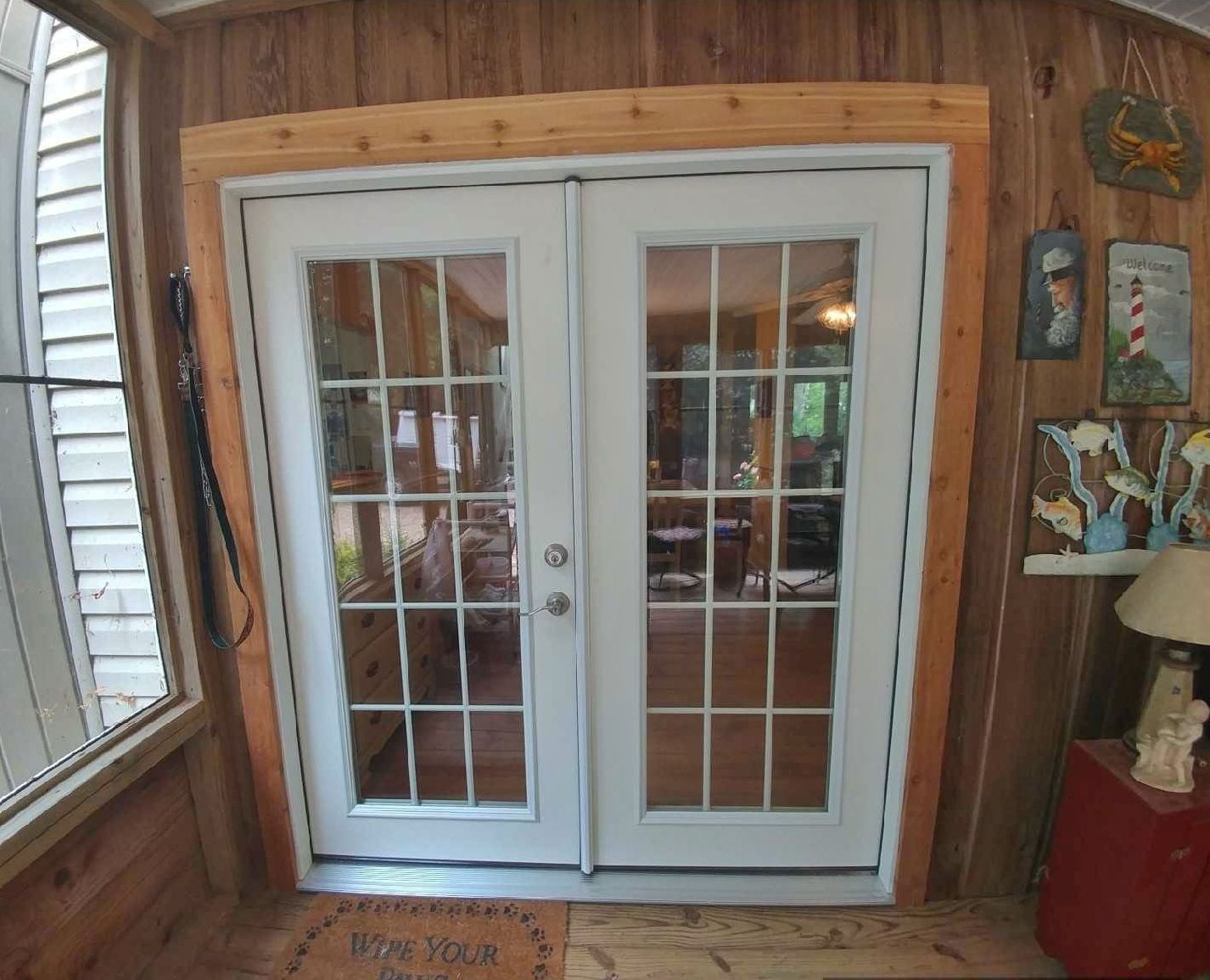 White French doors with glass panes, framed by wood, lead into a room. The surrounding space is paneled with wood.