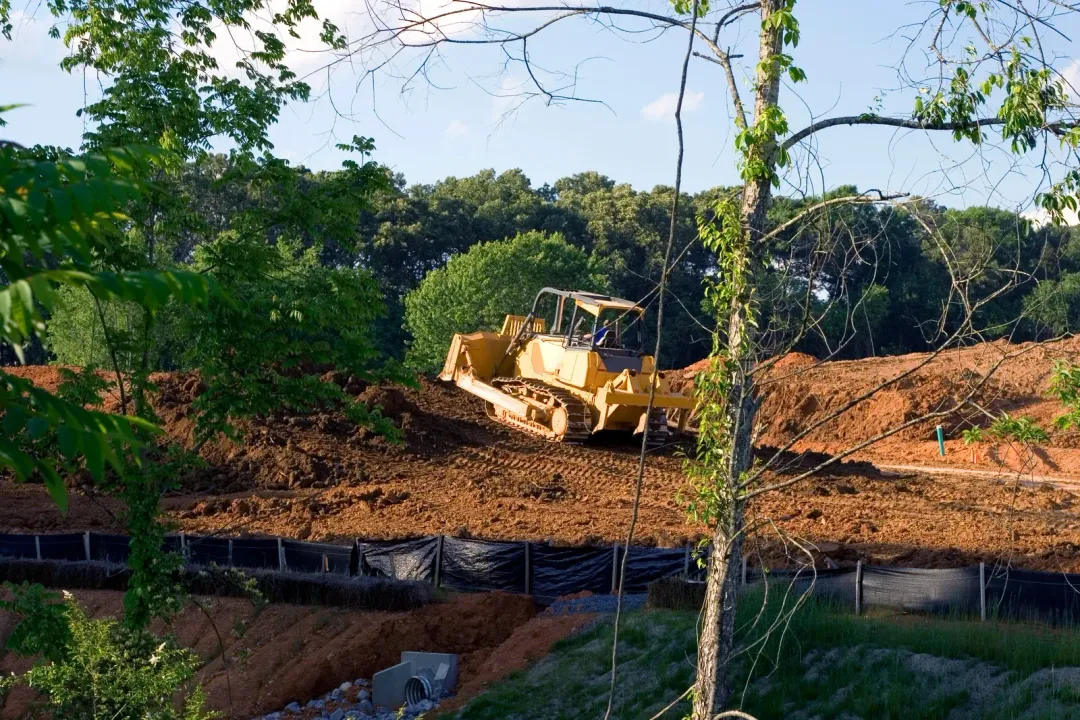 Yellow bulldozer on a dirt pile, clearing land near trees.