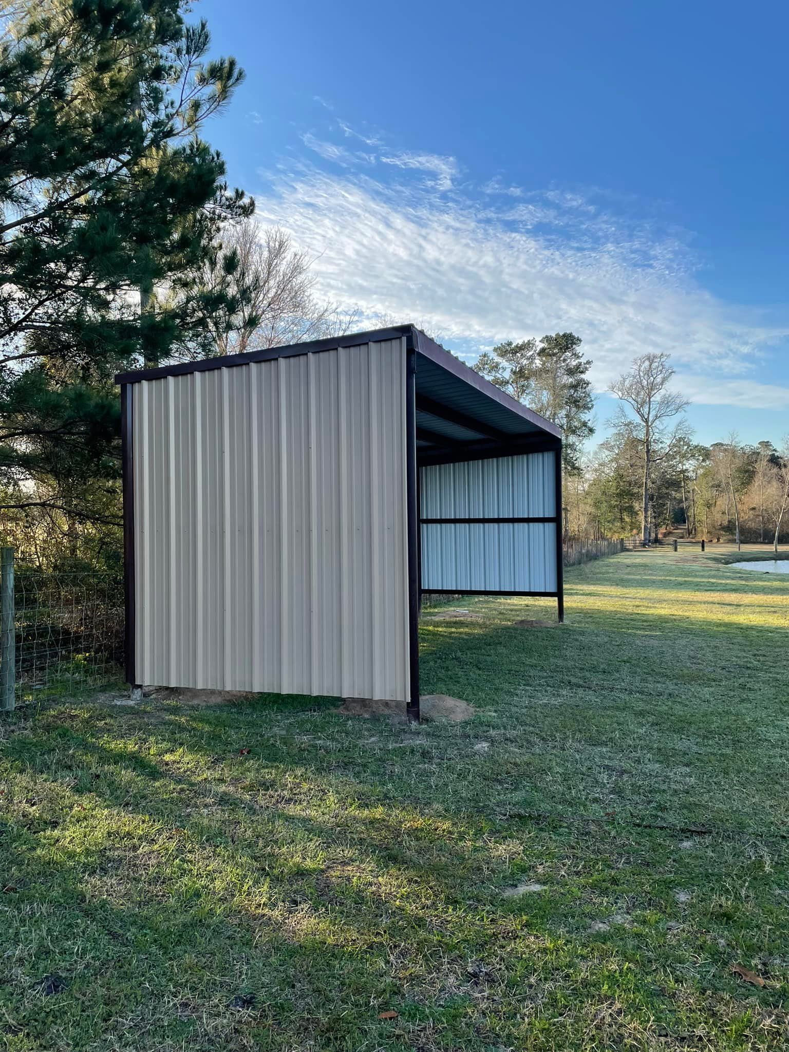 Tan metal shelter with a dark brown trim in a grassy field under a blue sky with clouds.