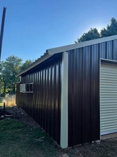 Brown metal building with a cream-colored trim under a blue sky with trees.