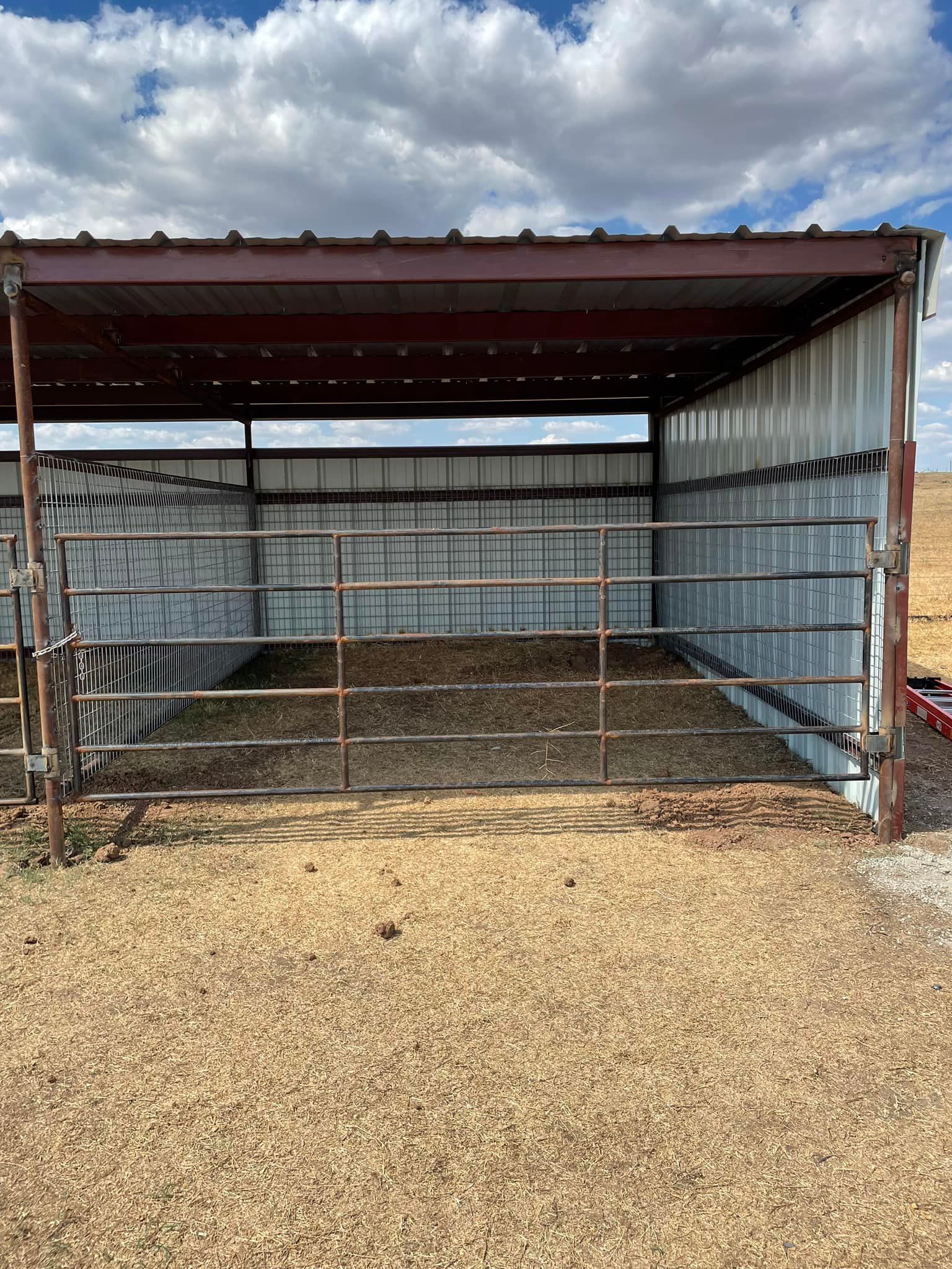 A metal shed with an open front, filled with hay, in a gravel lot.