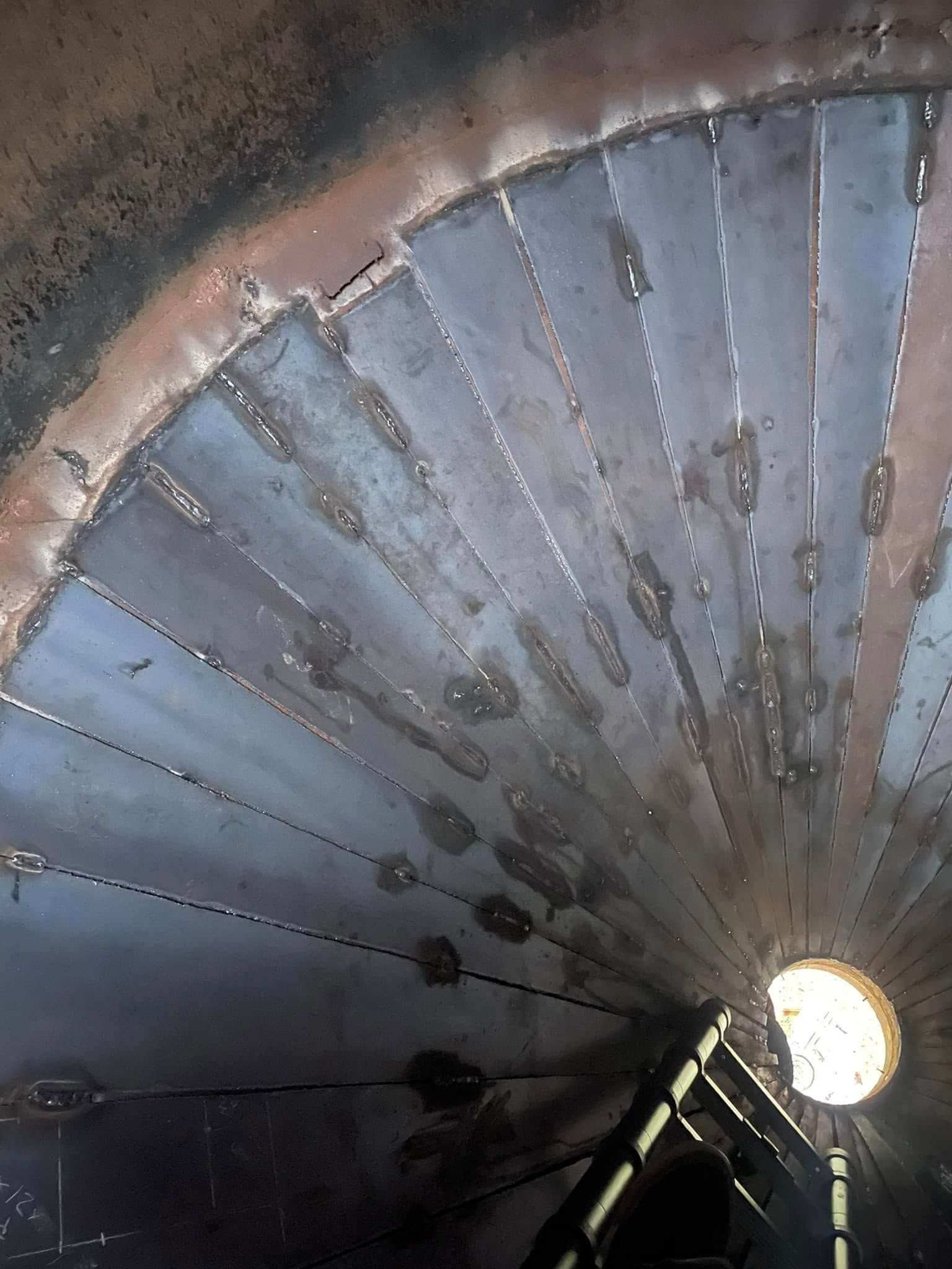 Inside of a metal container, showing welded panels radiating from a central opening, with light illuminating the interior.