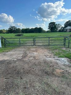 Metal gate opens to a grassy field under a blue sky.
