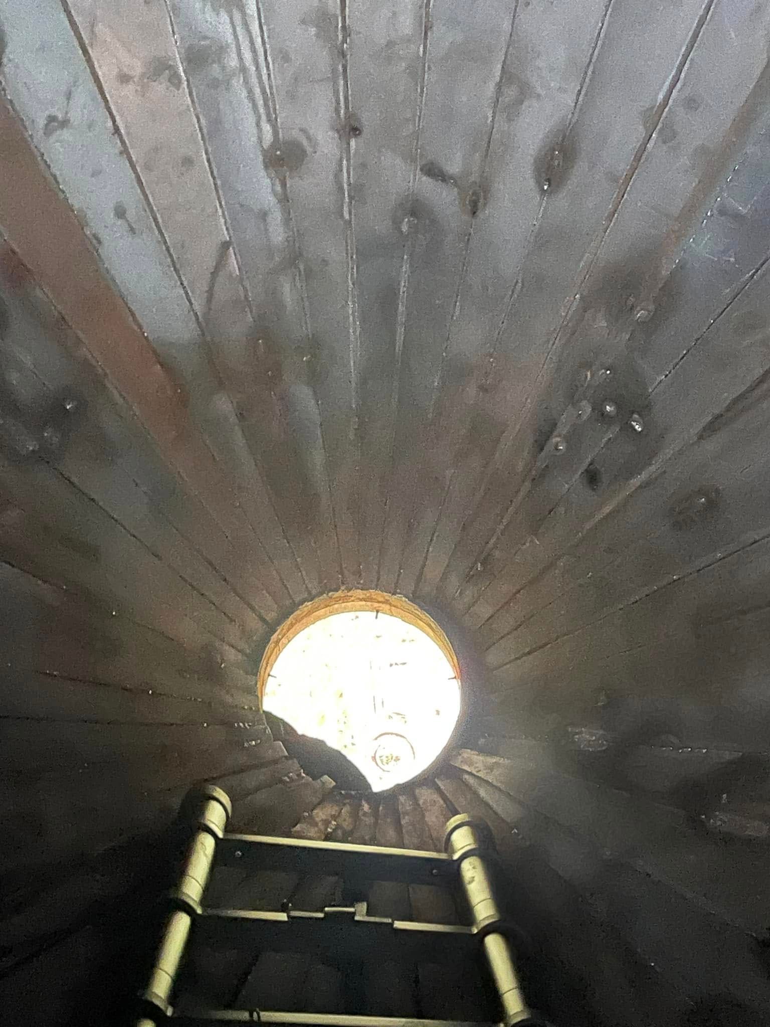 Looking up through a circular opening in a wooden ceiling, ladder reaching up.