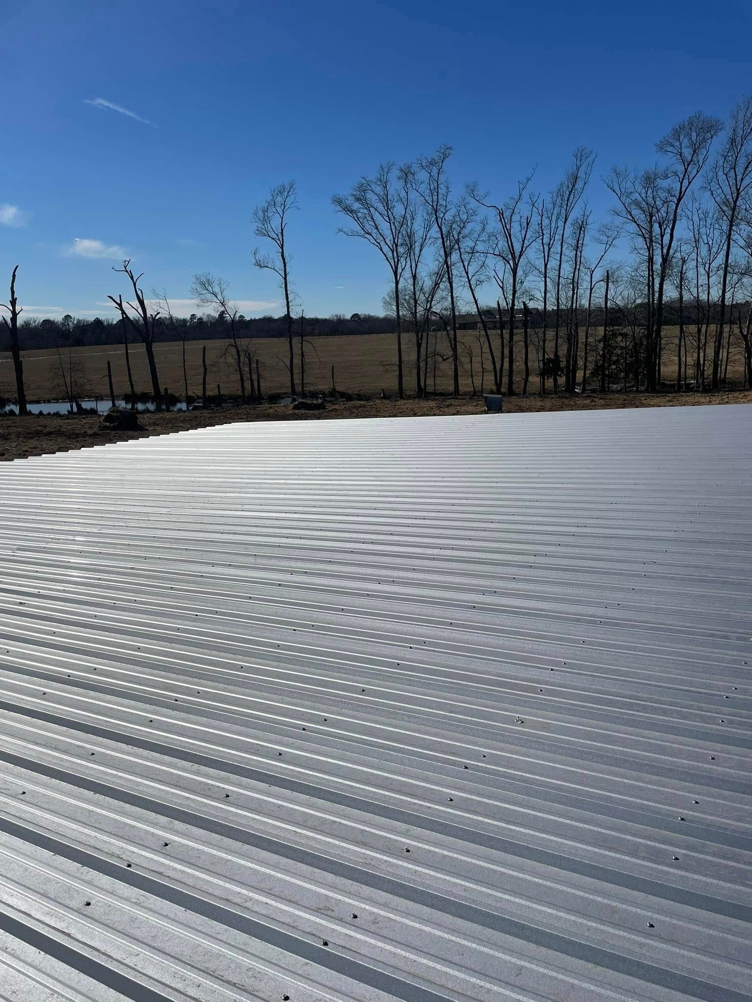 Large, flat, corrugated metal surface outdoors under a blue sky, with trees in the distance.