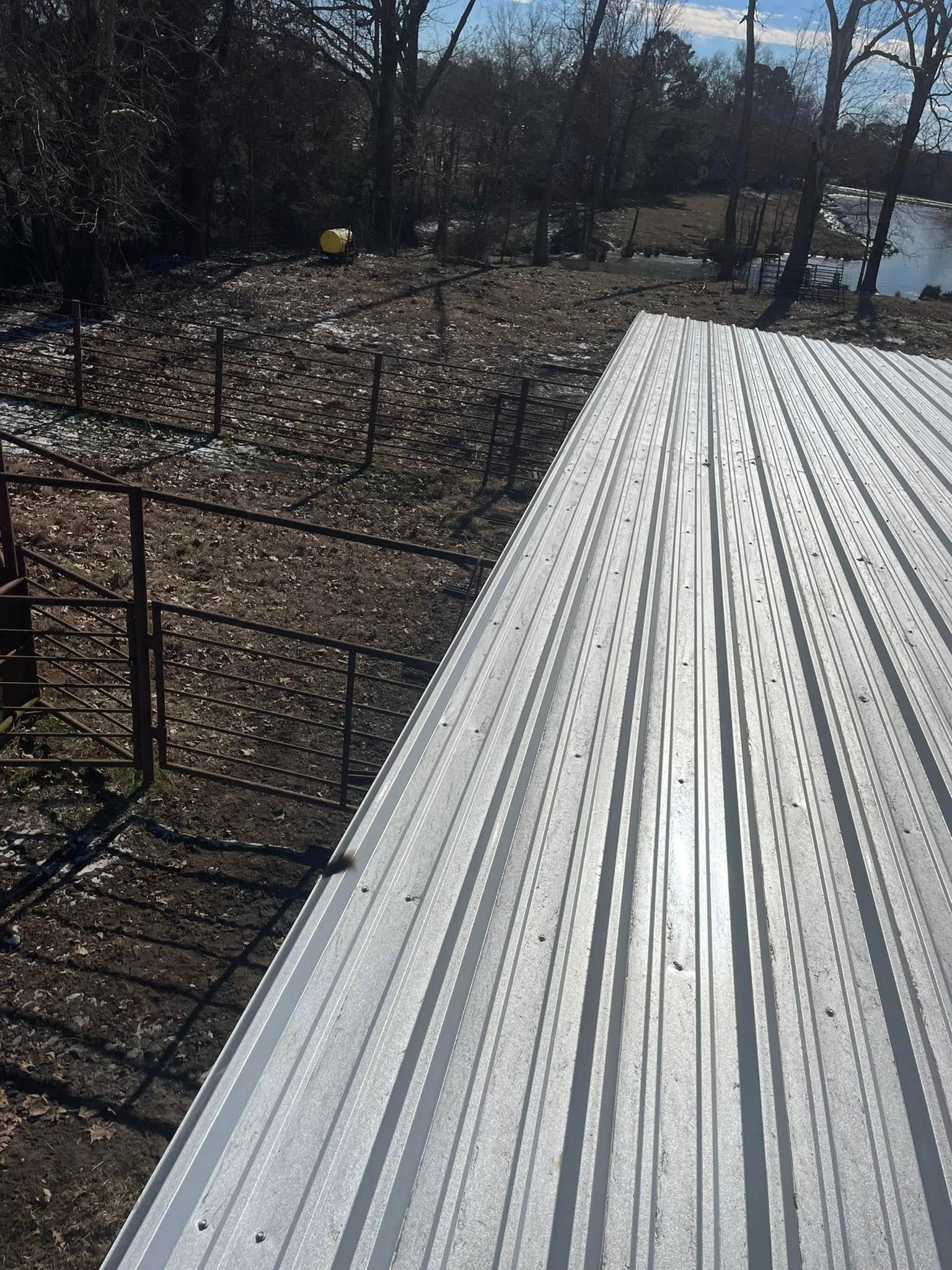 Metal roof edge with dark fencing and a field, near a pond and trees.