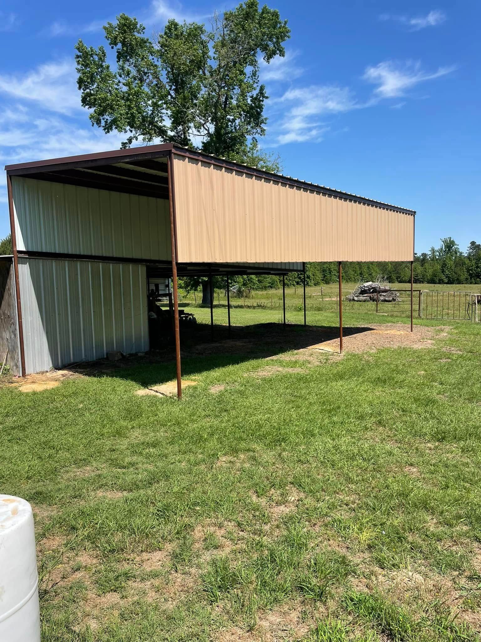 A metal carport with a tan roof and side, in a grassy field under a blue sky.