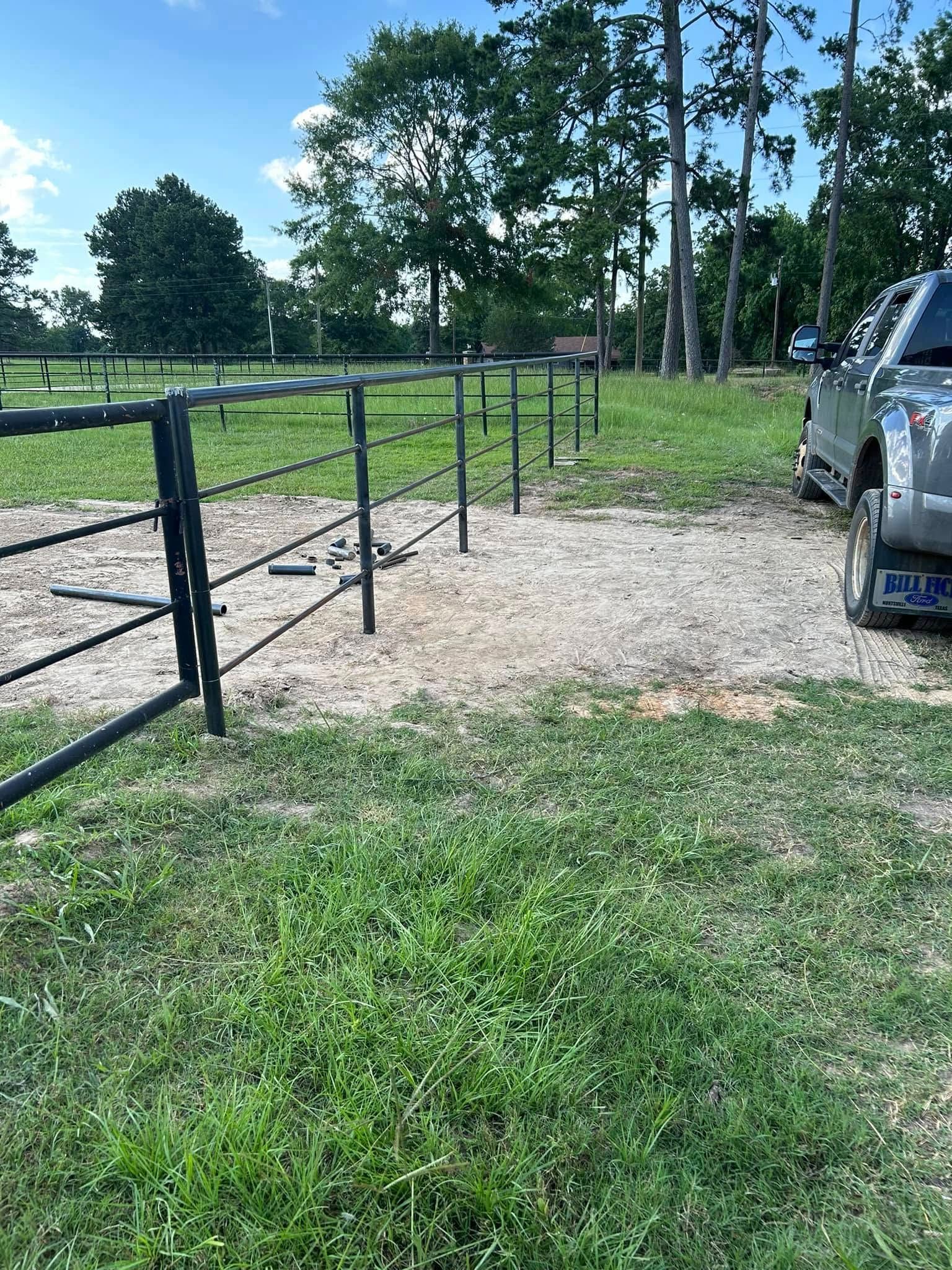 Green grass leads to a gravel area with a black metal fence, and a truck is parked nearby.