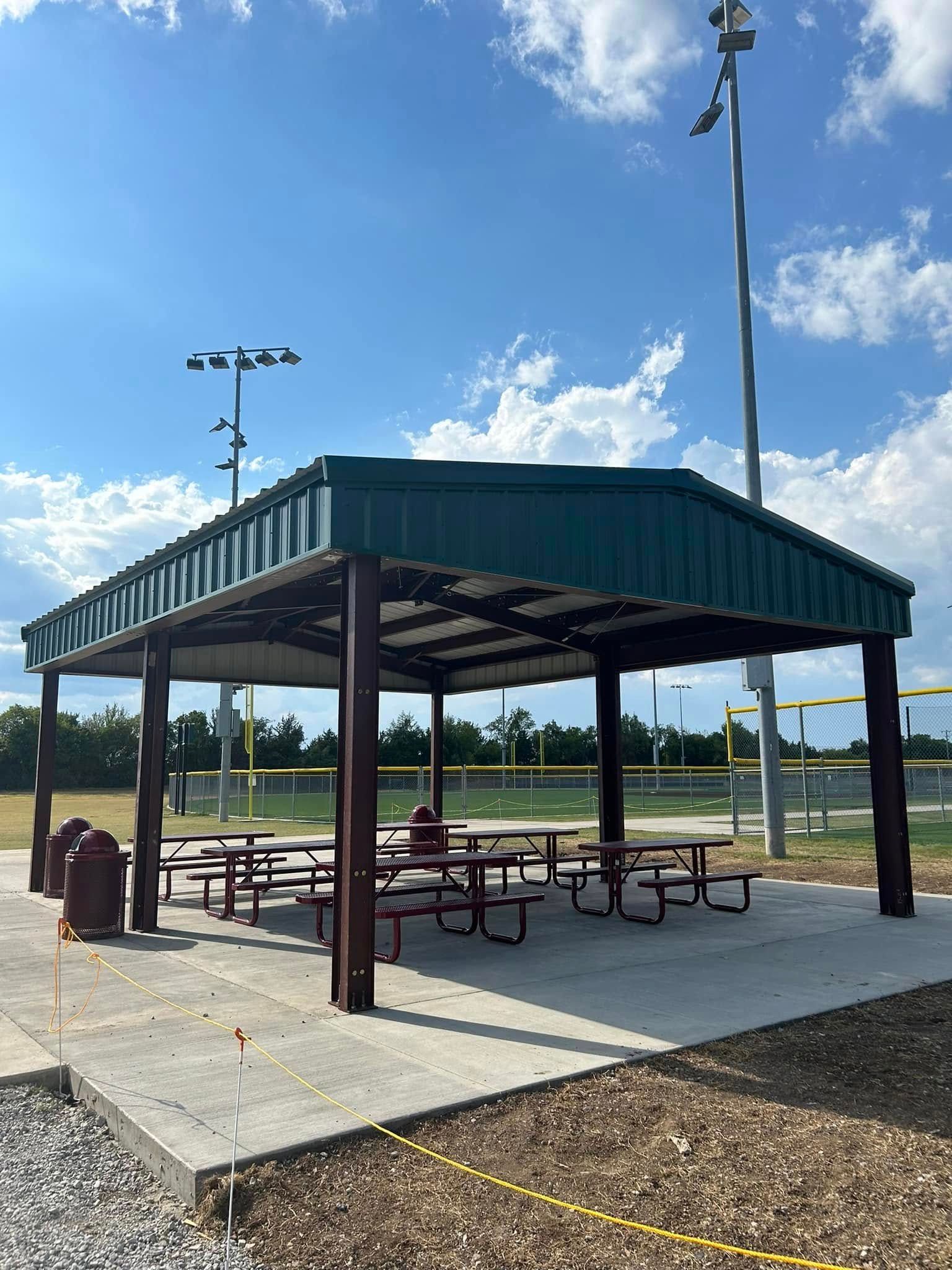 Covered picnic area with tables on a concrete pad at a baseball field.