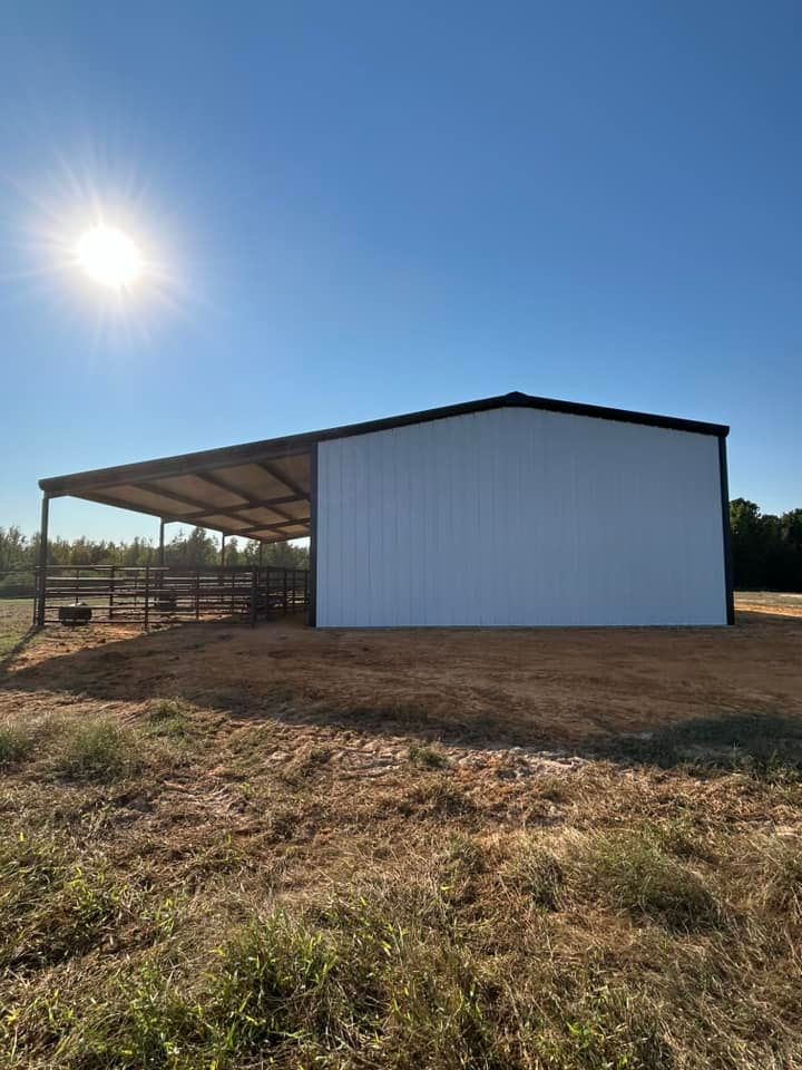A white metal barn with a covered area, on a sunny day in a grassy field.