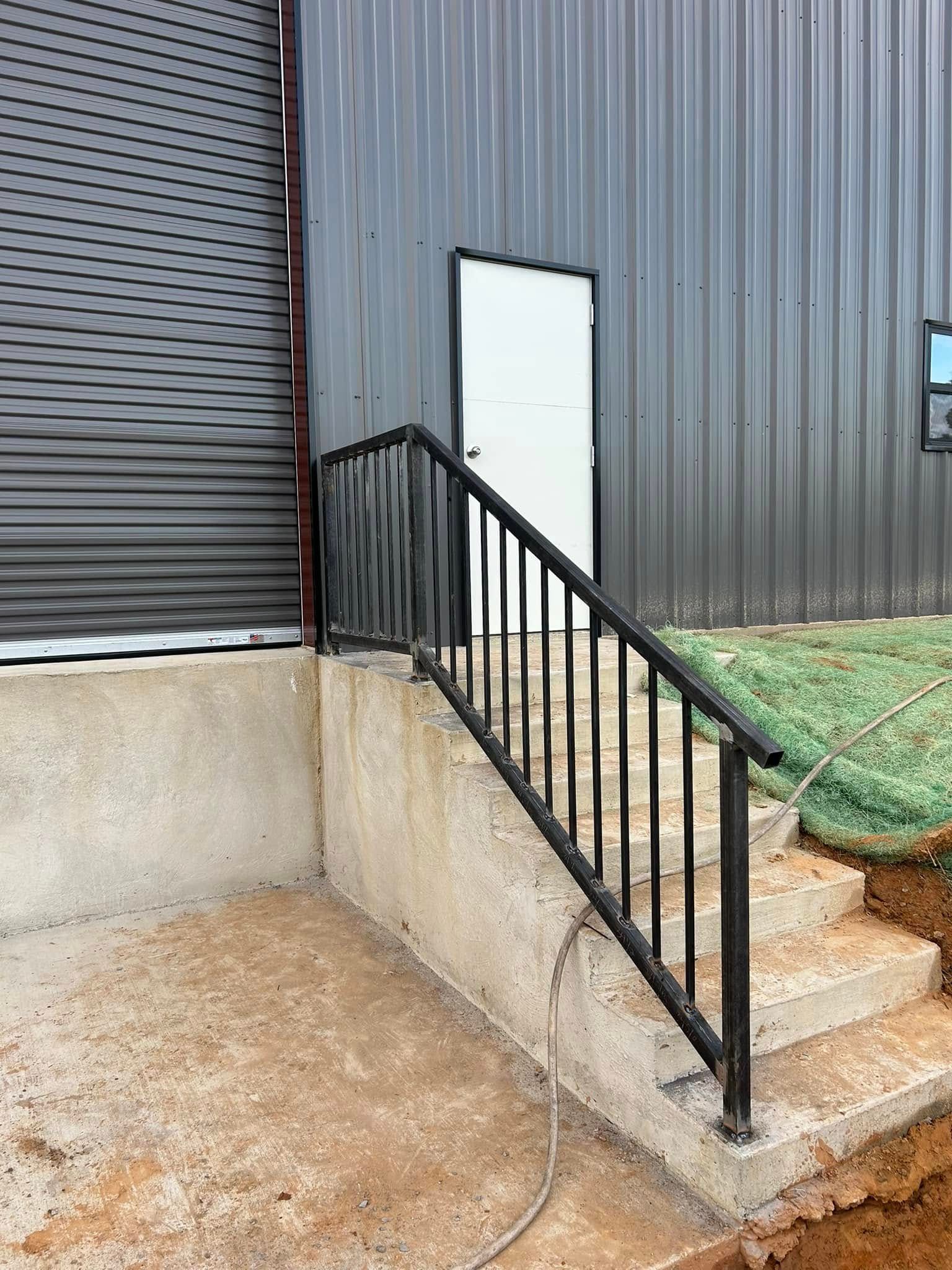 Black metal handrail and steps leading to a white door on a gray building.