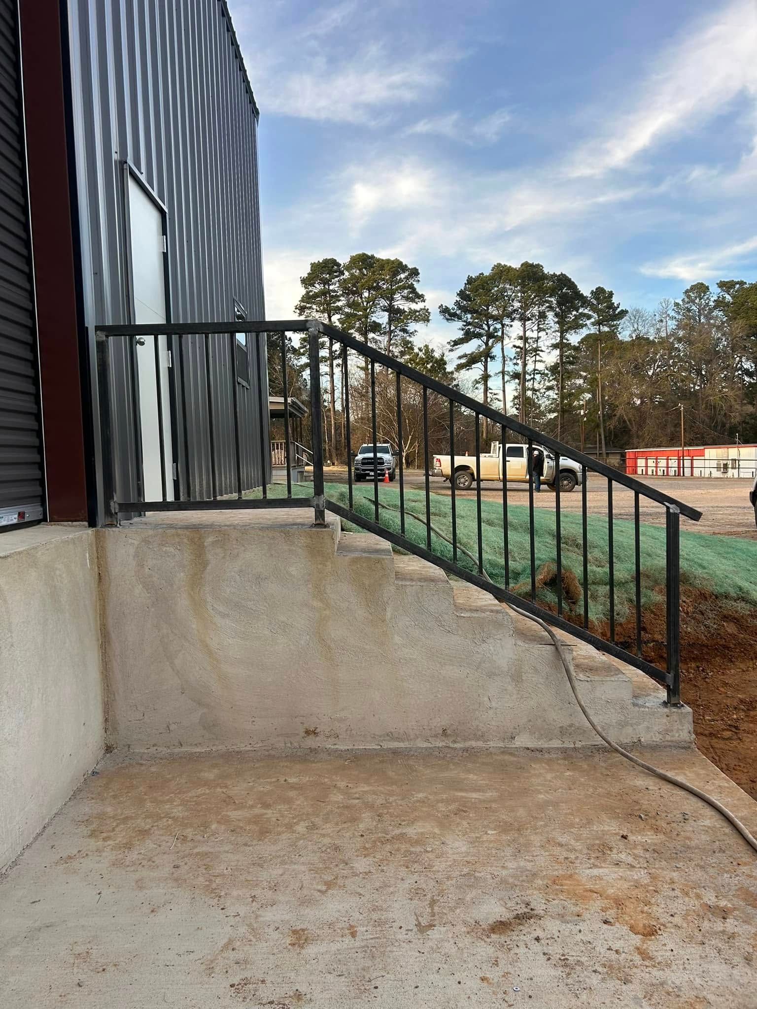 Exterior view of a building with a concrete staircase, metal railing, and a cloudy sky.