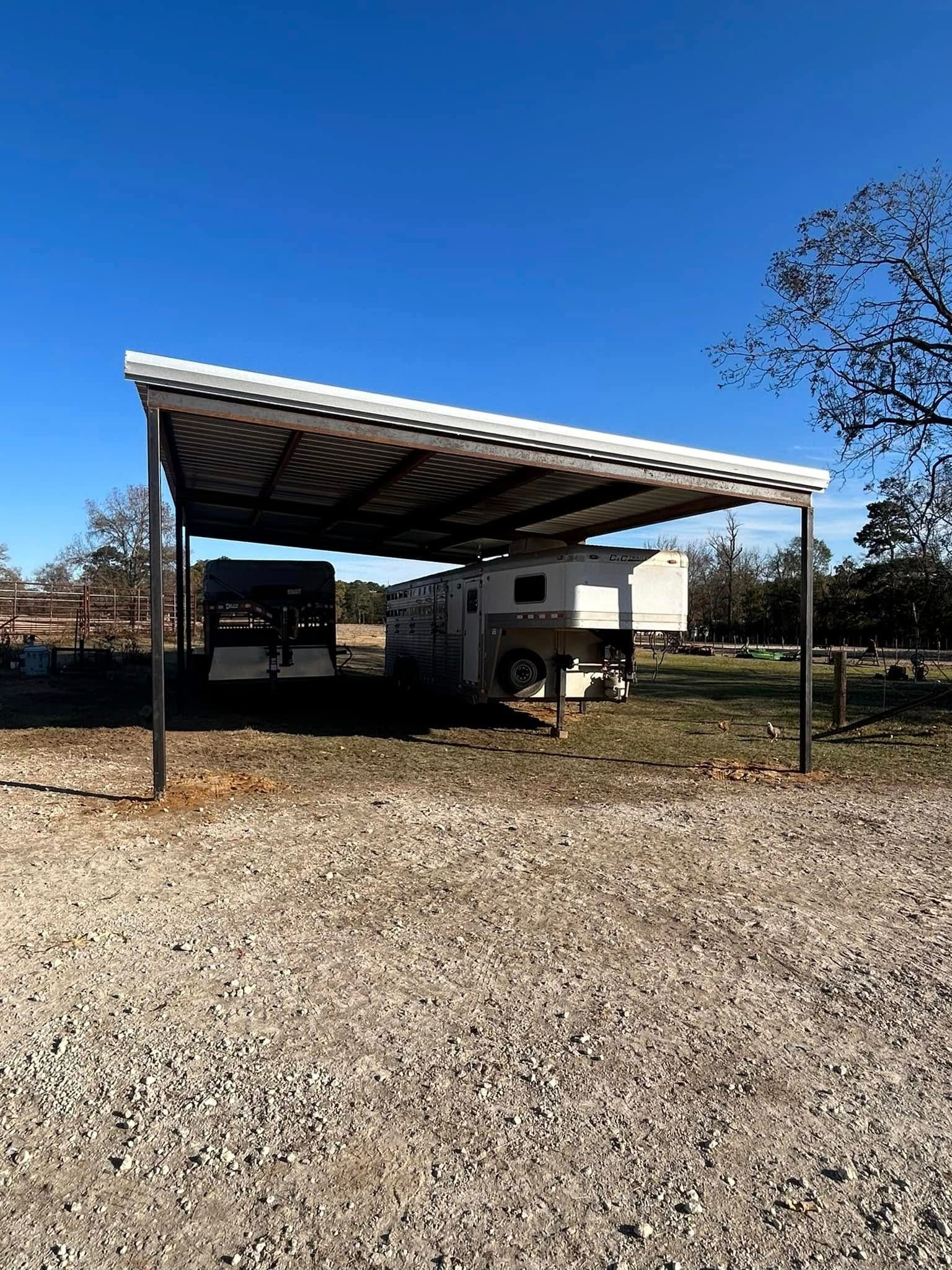 A canopy shades two trailers on a gravel lot under a clear blue sky.