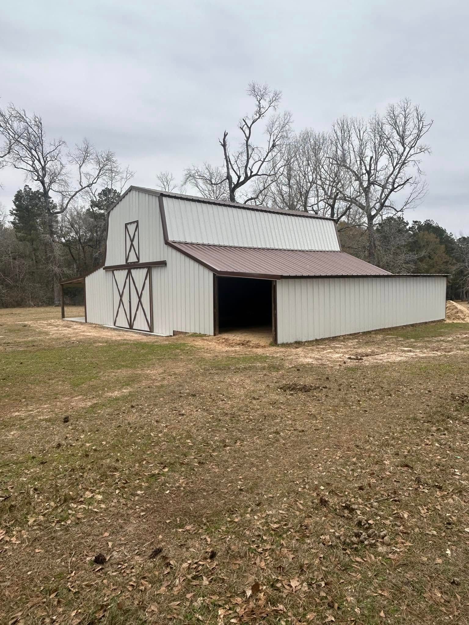 White barn with brown roof and doors, in a field, under a cloudy sky.