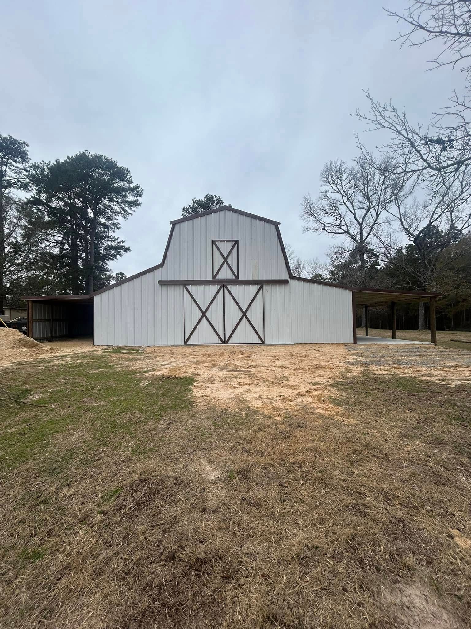 White barn with black accents, standing in a field, under an overcast sky.