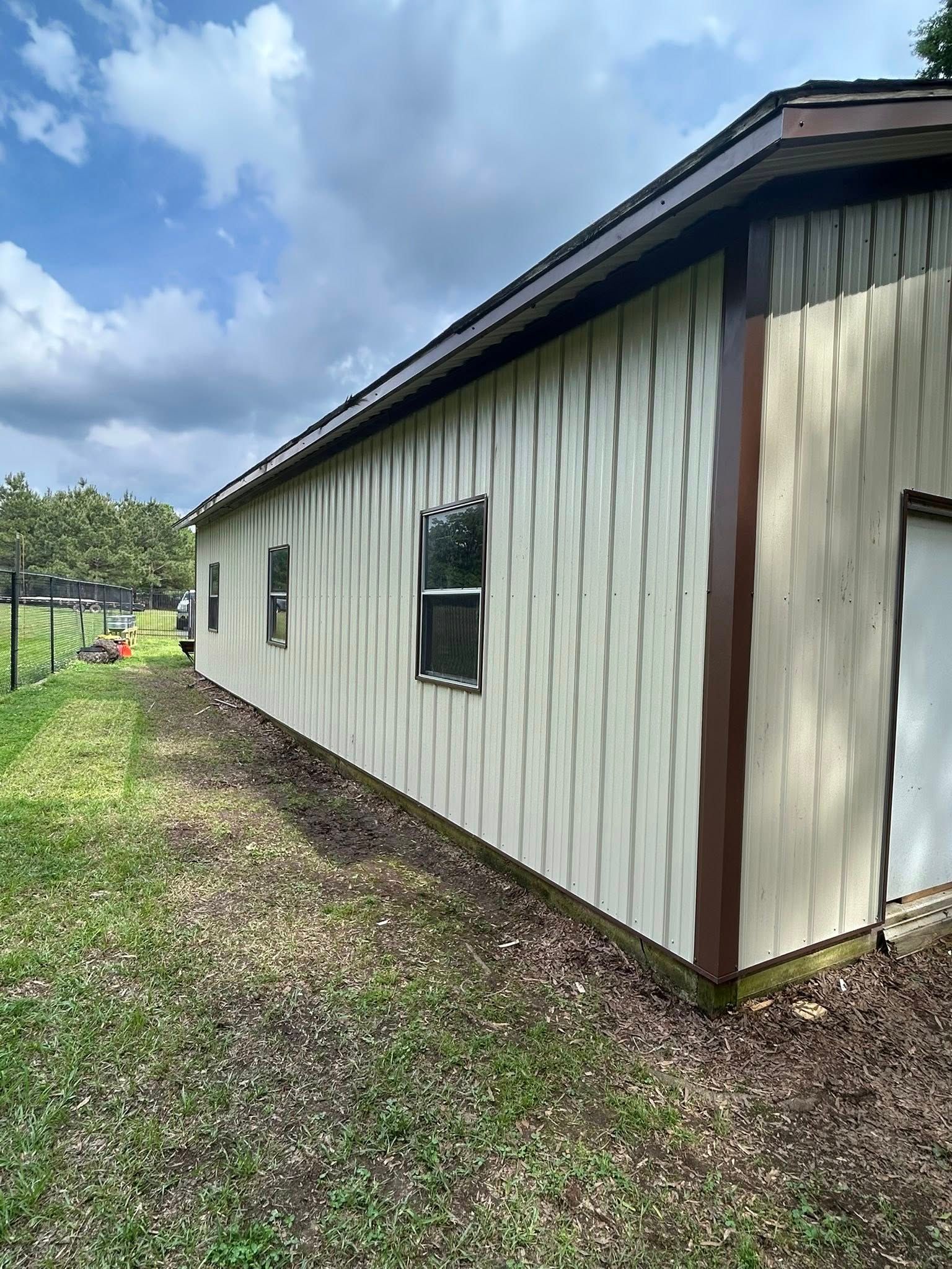 Side view of a beige building with brown trim, three windows, and a door on a grassy lawn.