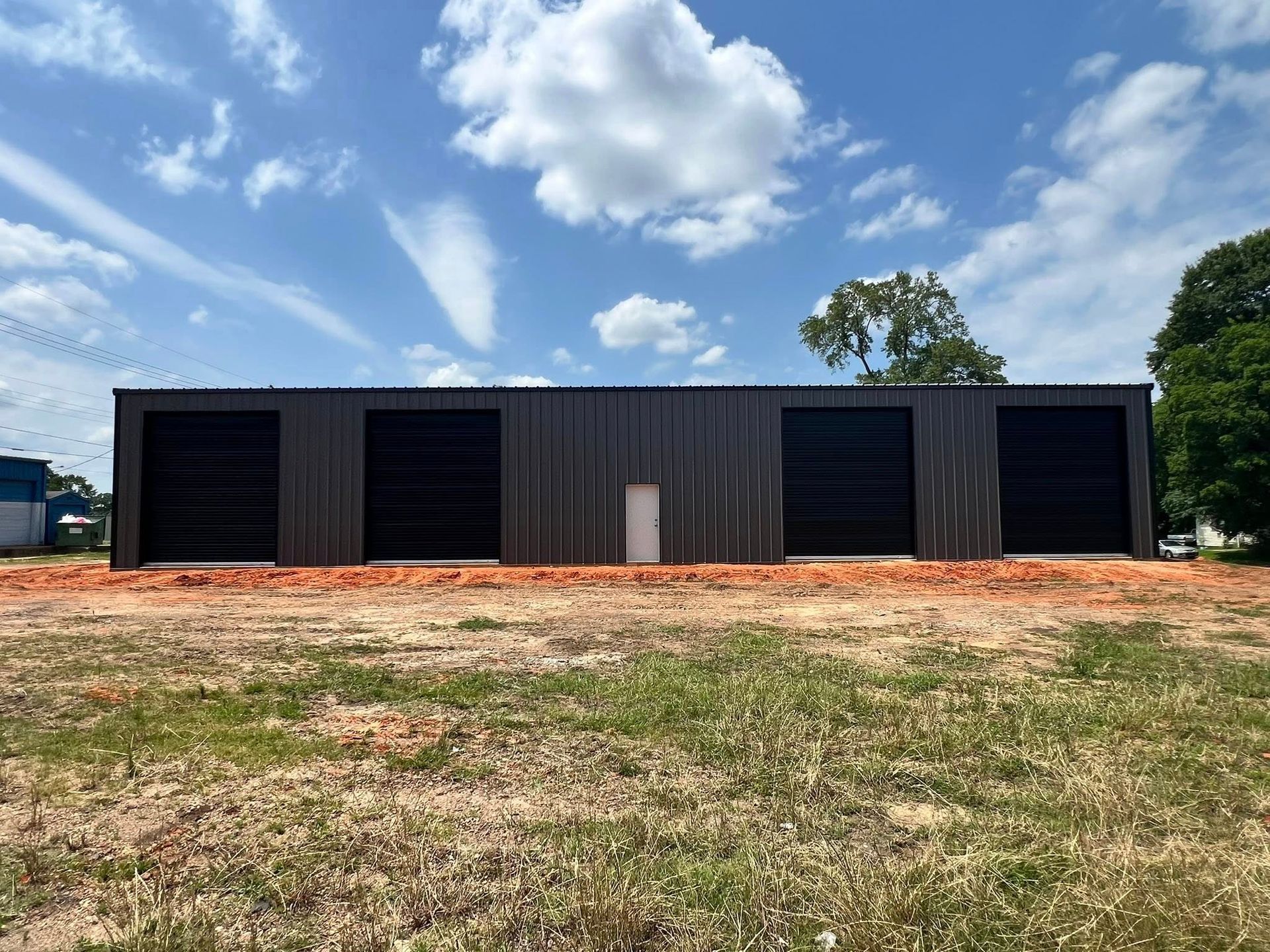 Brown metal storage building with four bays and a white door, under a blue sky.