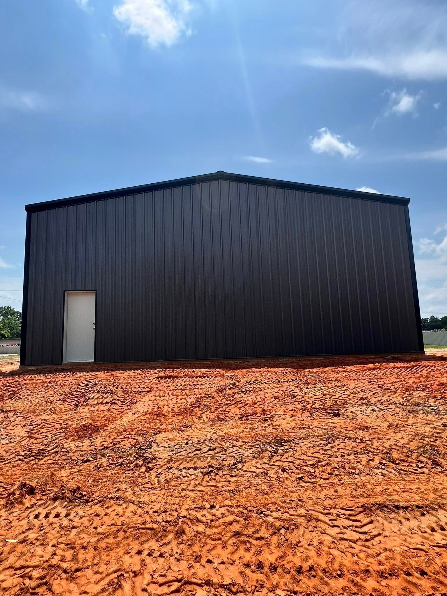 Black metal building with white door on red dirt under a blue sky.