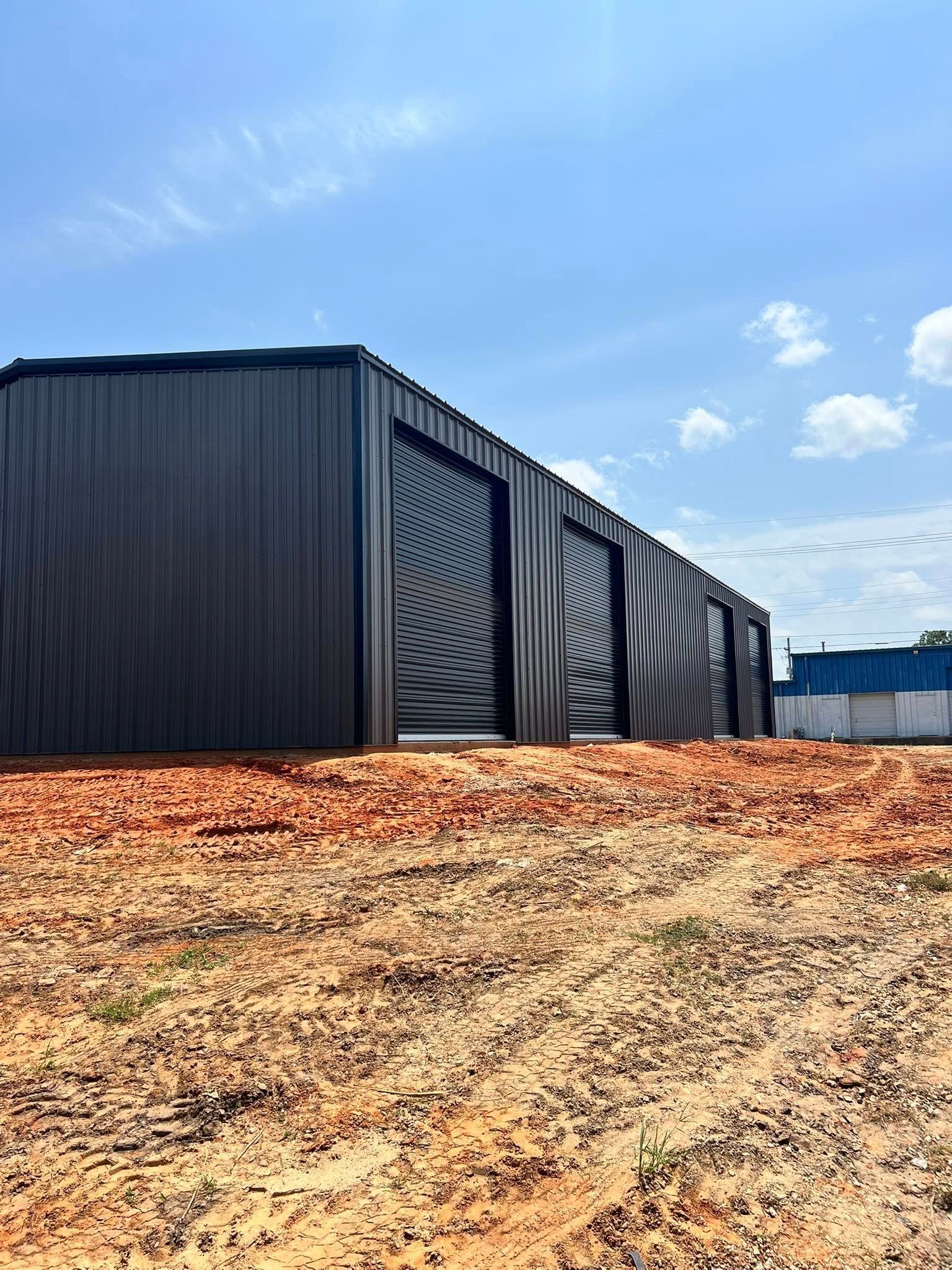 Black metal storage units on a red dirt lot under a partly cloudy blue sky.