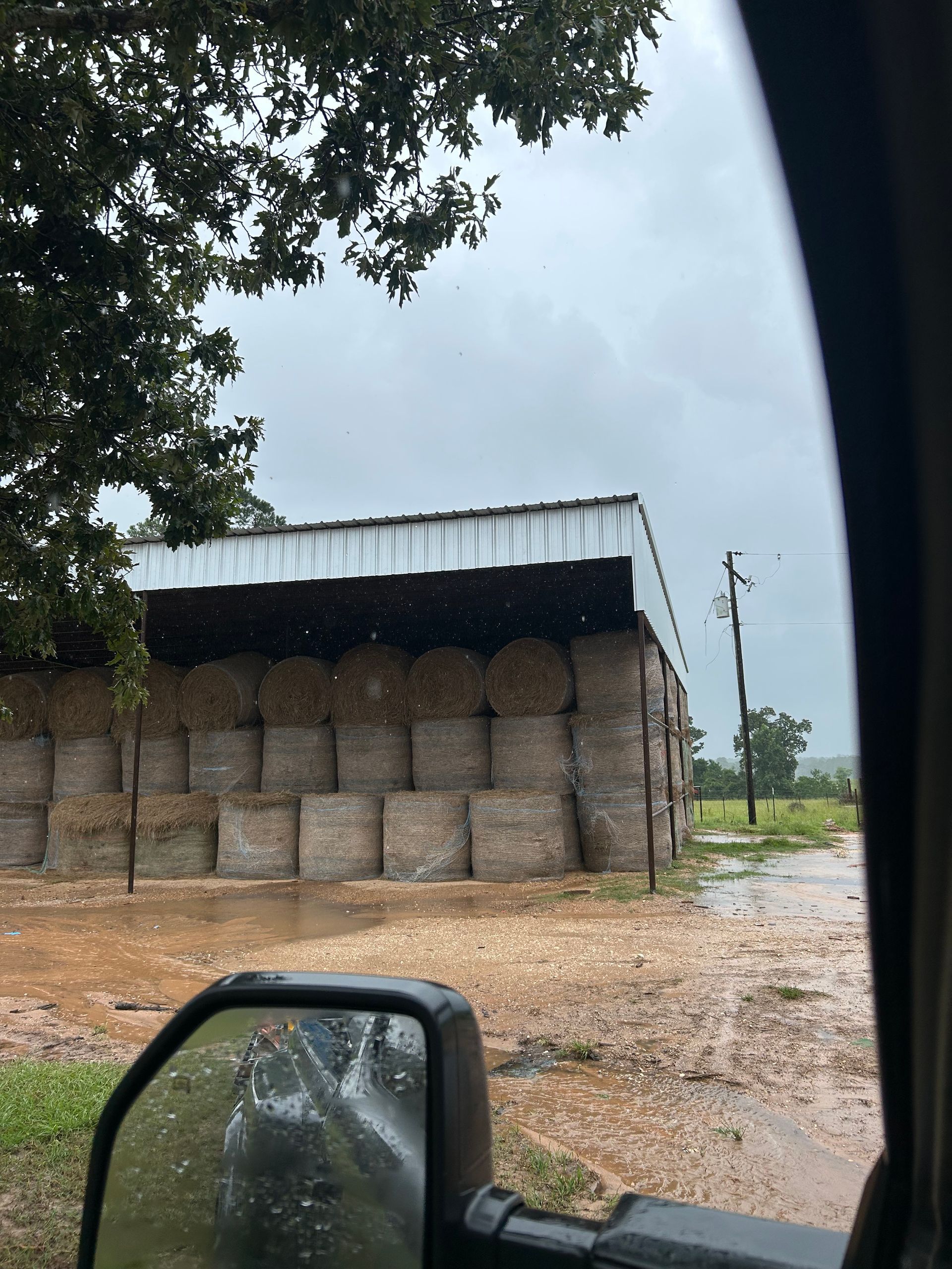 Rainy scene of hay bales stacked in a barn, viewed from a vehicle.