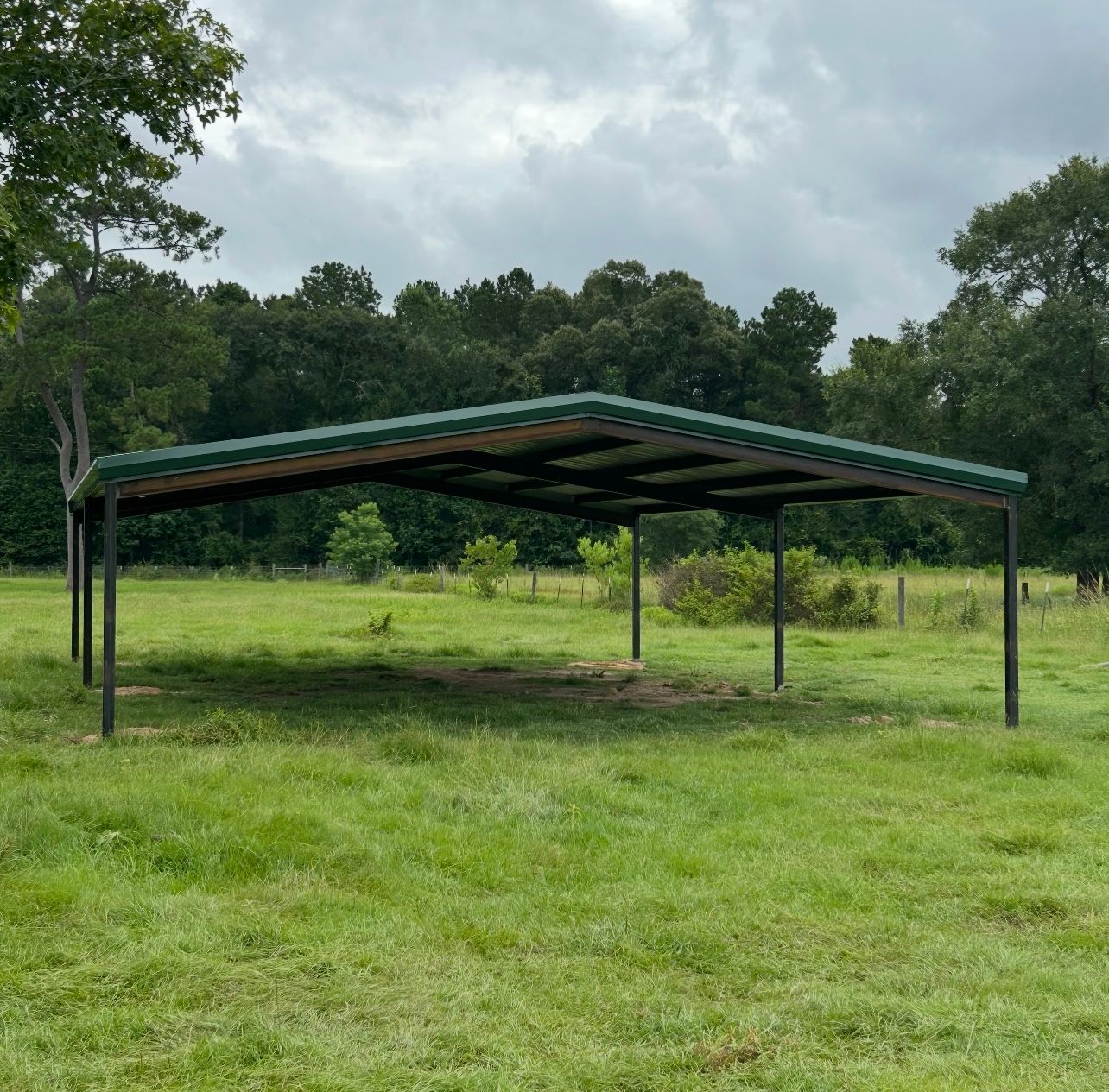 Metal carport in a grassy field with a treeline in the background.