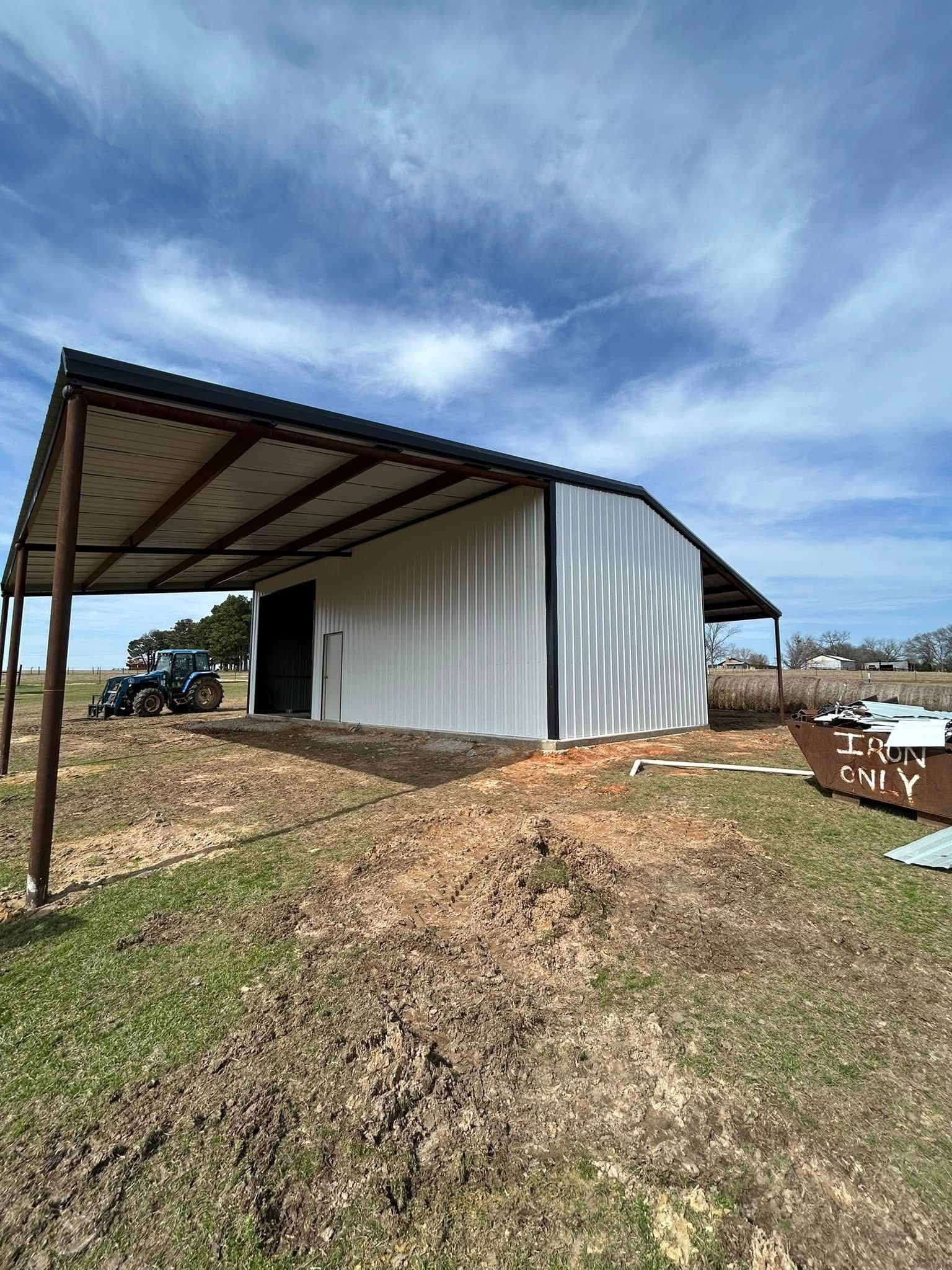 White metal barn with black trim and a brown awning under a cloudy sky.