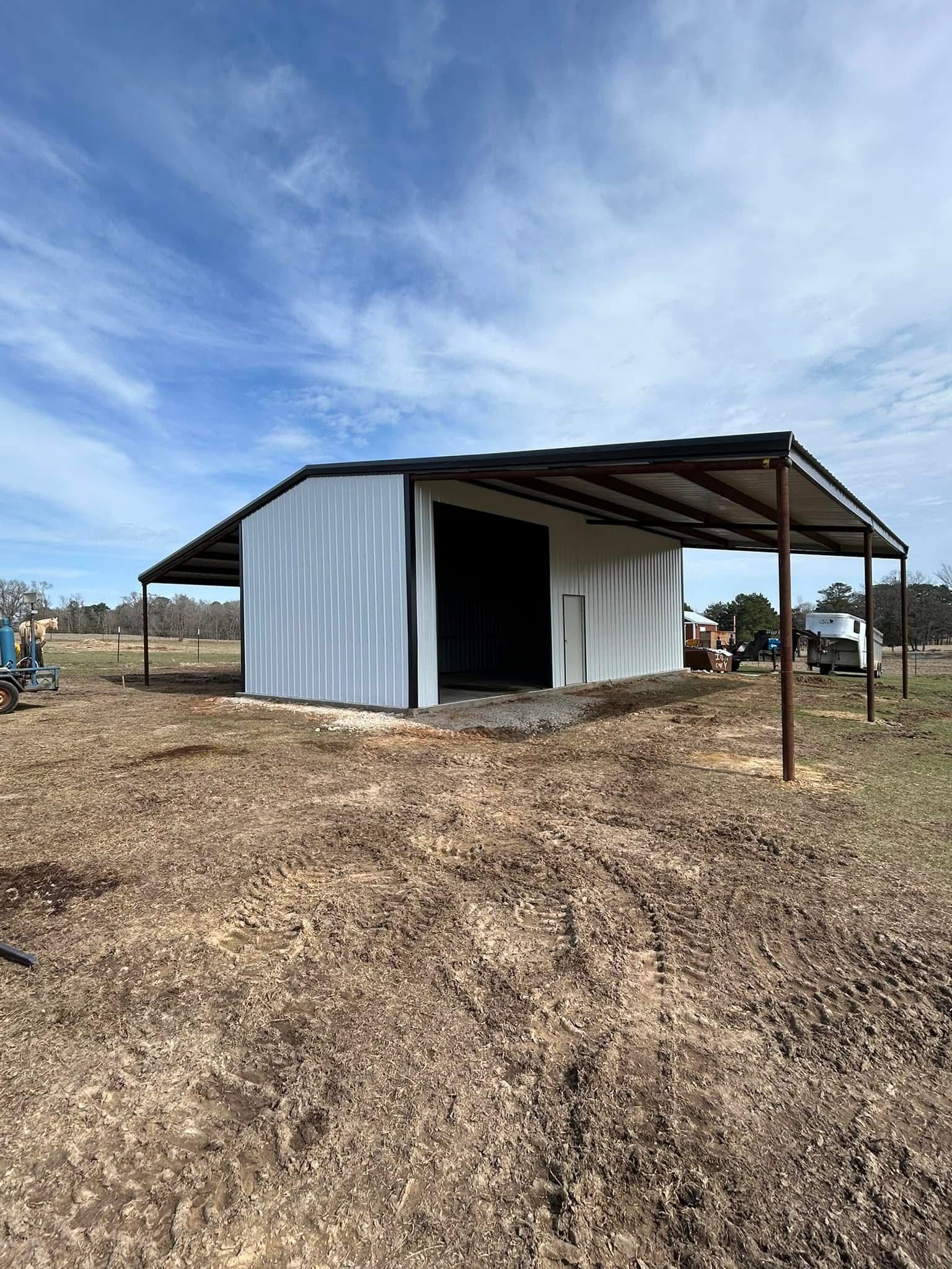 White metal barn with a brown roof and supports under a blue sky.