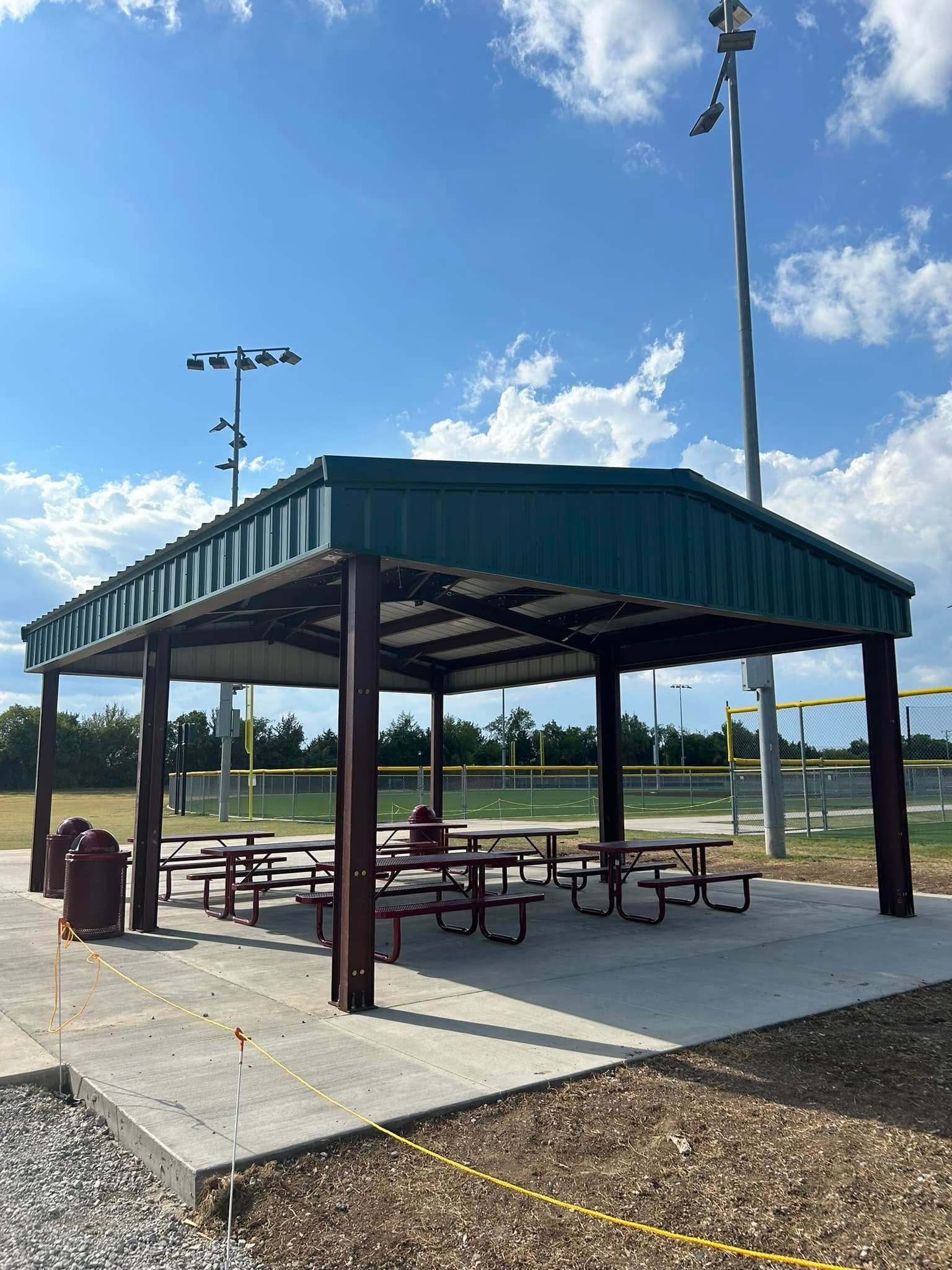 Picnic shelter with tables at a baseball field under a blue sky.